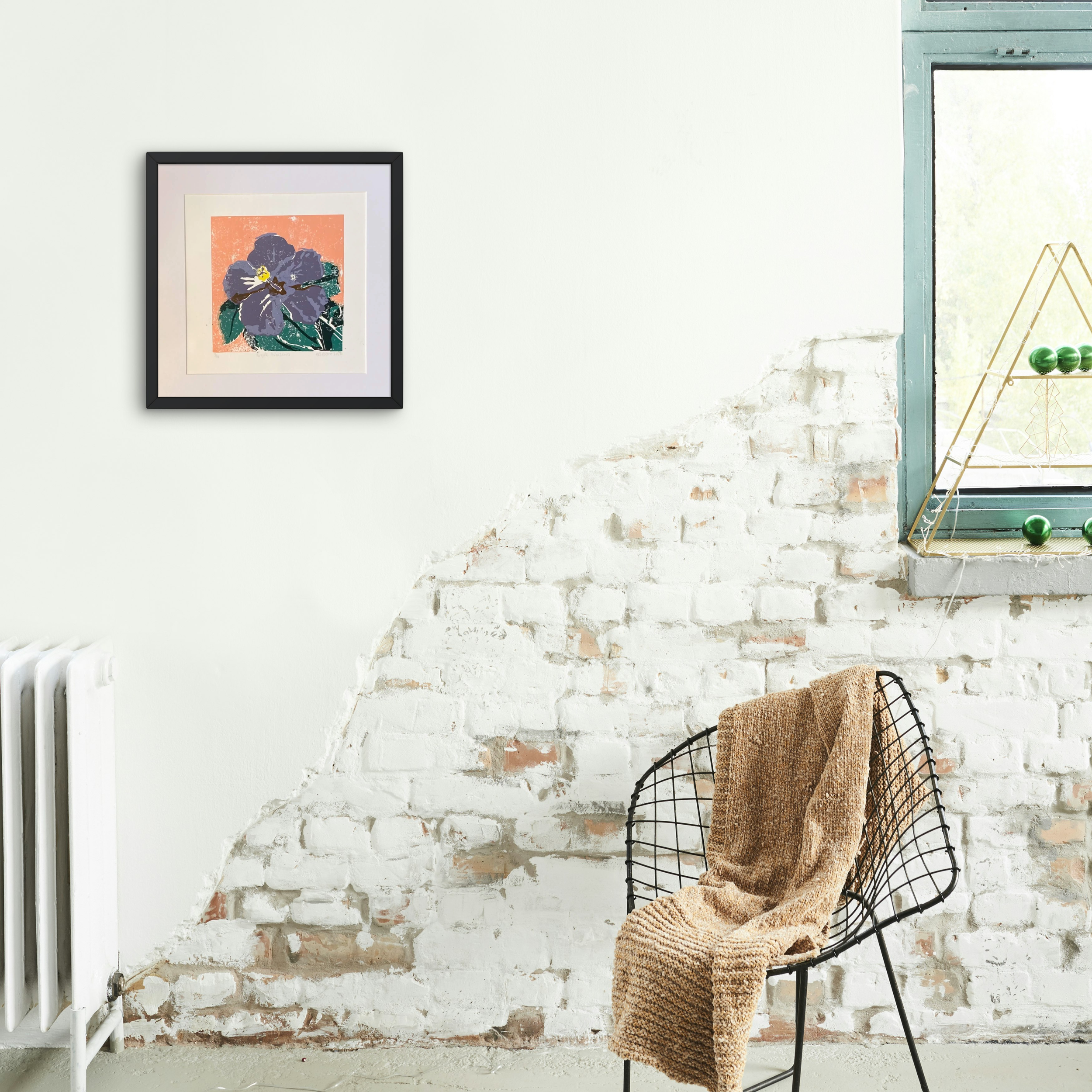 Purple Hibiscus Original Linocut in black frame on white plaster wall next to exposed brick and wire framed chair.png
