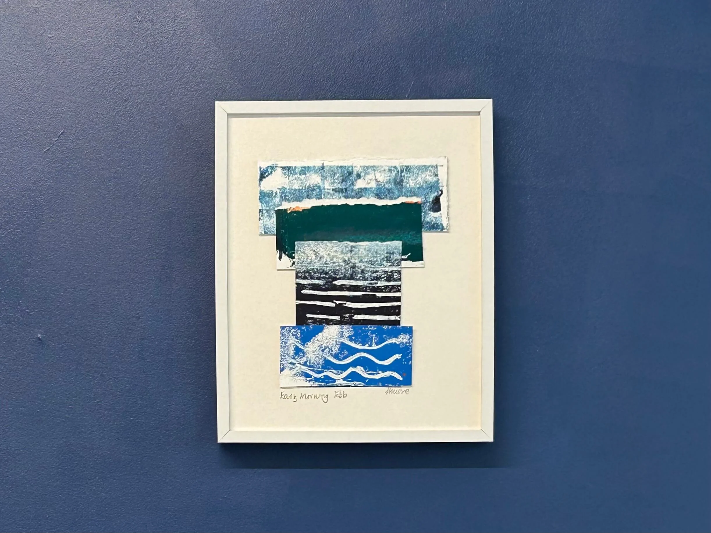 Blue mixed media collage and print in white frame on navy wall