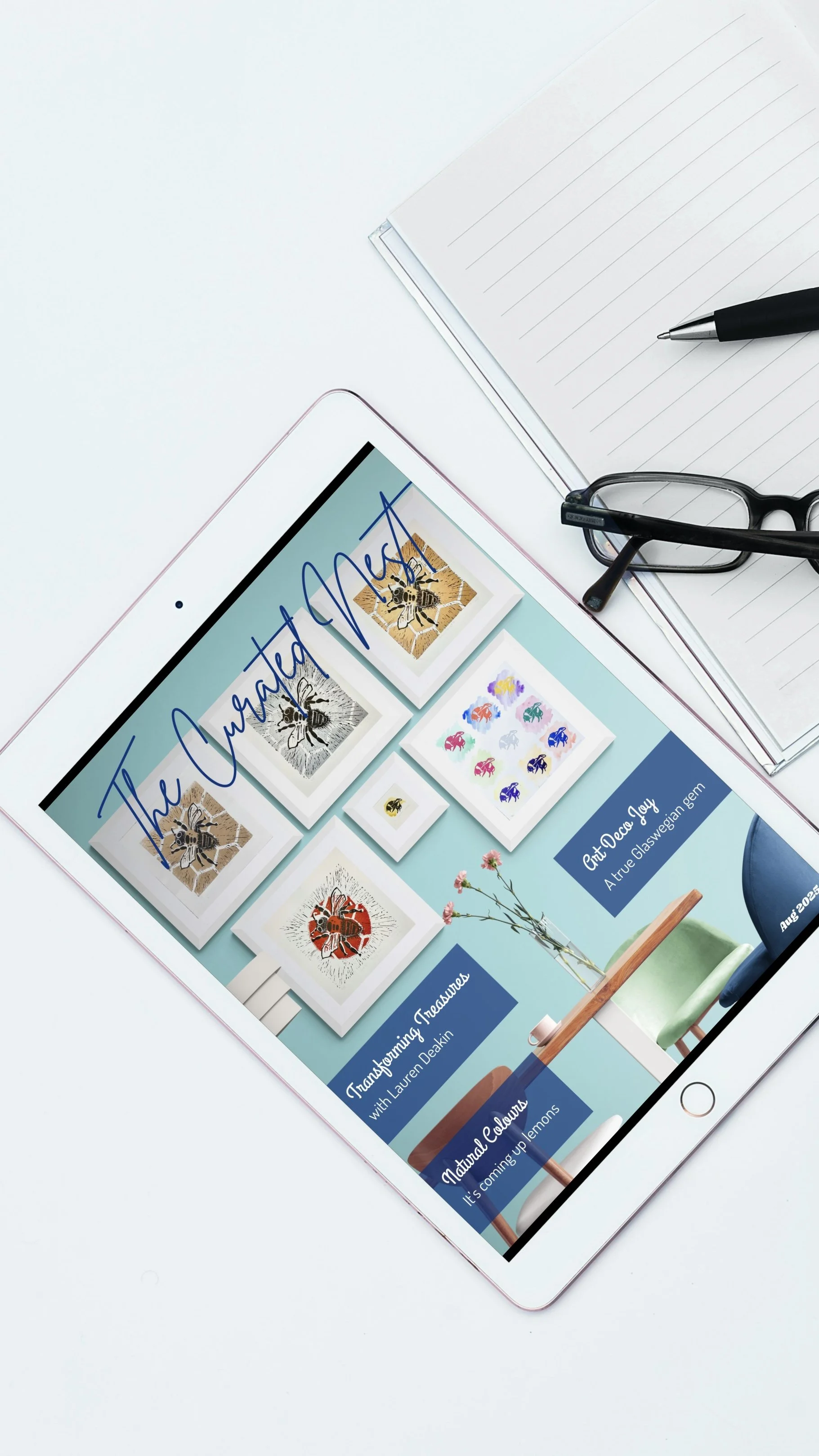 Digital tablet displaying a title "The Curated Nest" with images of bees and other insects, placed on a white desk with a notebook, pen, and glasses nearby.