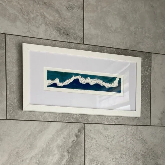 A Slice of Heaven sea wave linocut in white frame in bathroom with grey tiles