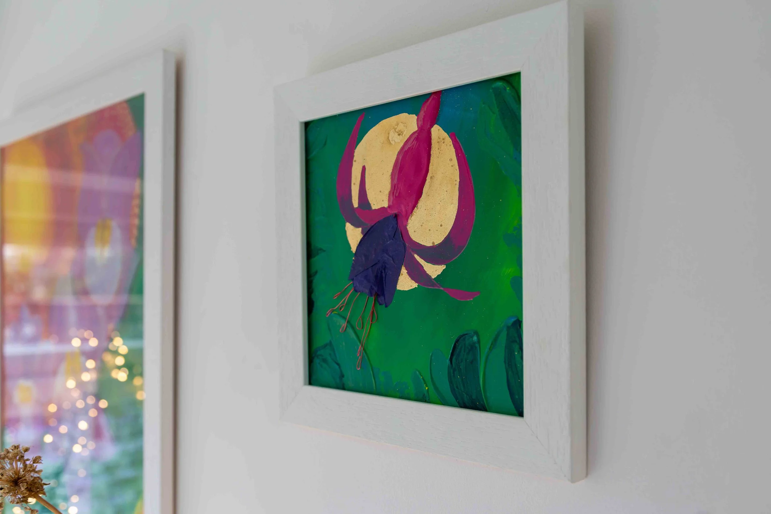 Fuchsia mixed media art in a white frame on a studio wall with other artworks in the distance