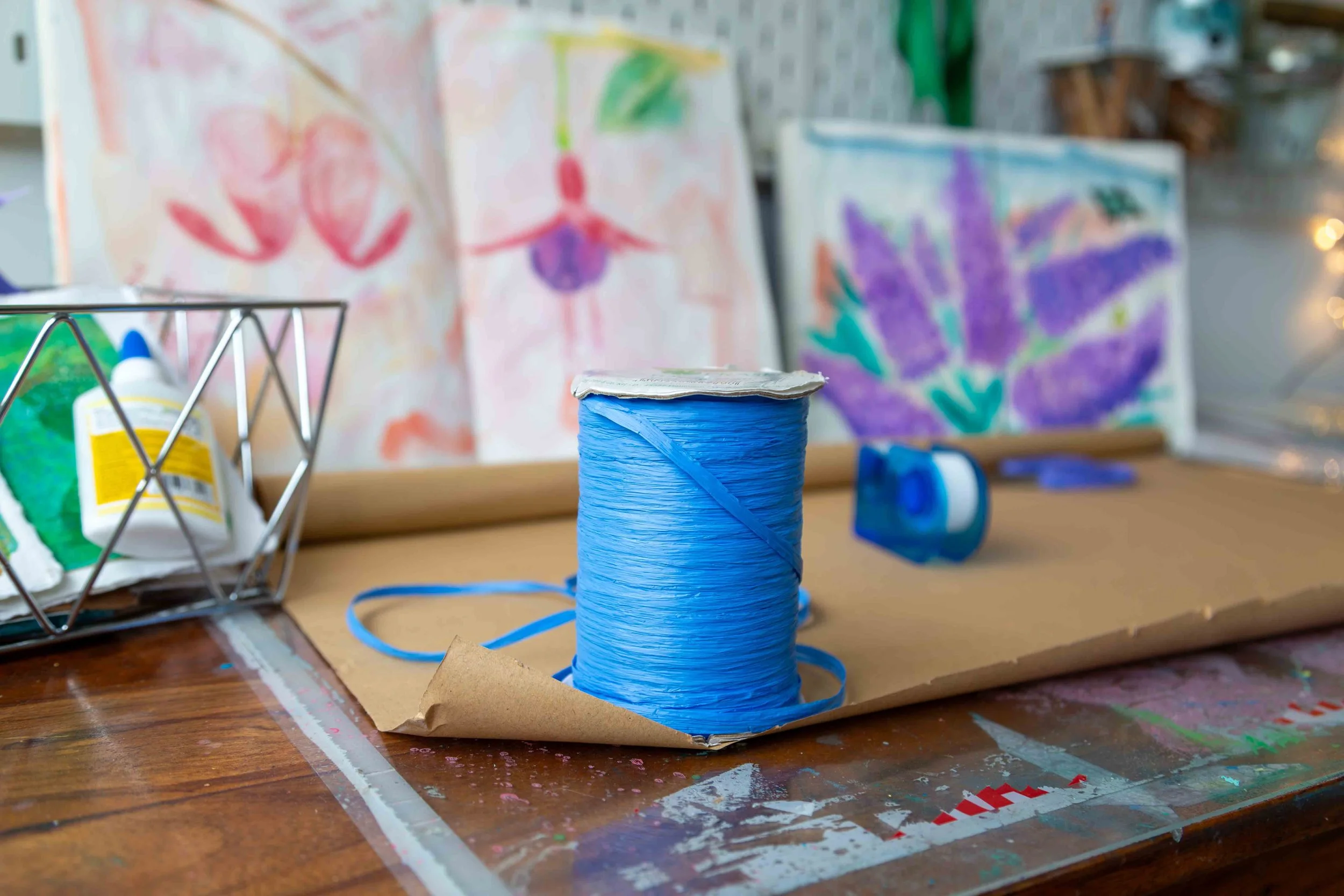 Blue raffia, brown paper and scissor on a wooden artist's desk with floral sketches on display