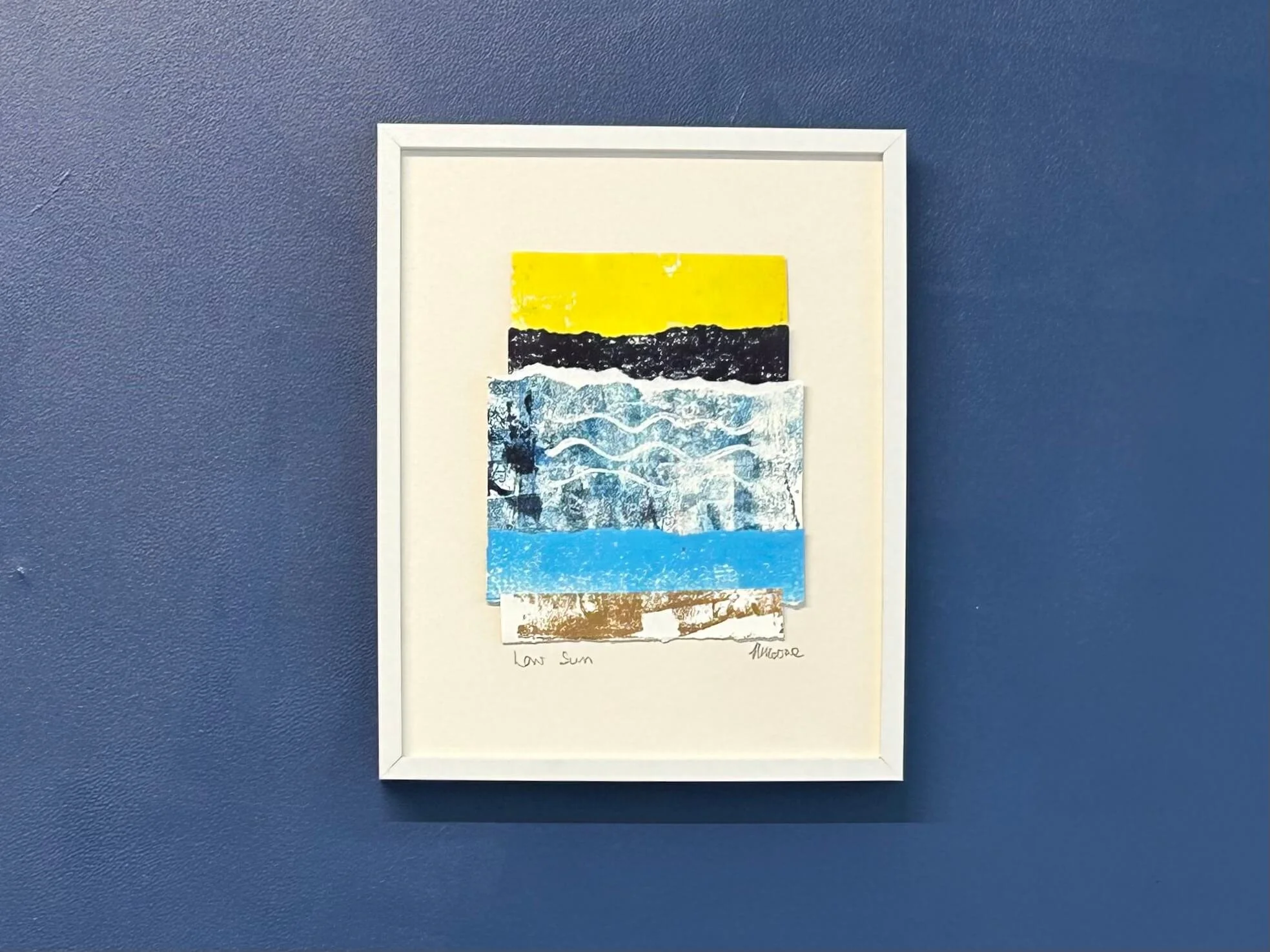 Yellow and blue mixed media collage and print in white frame on navy wall