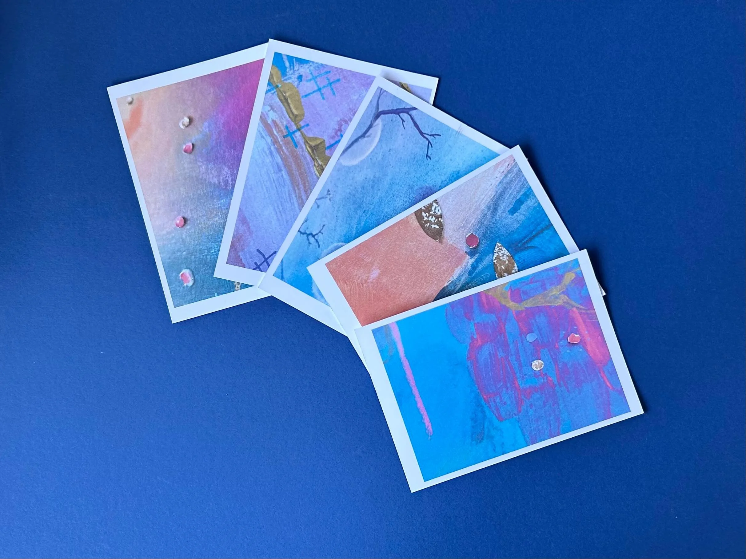 5 art postcards in vibrant colours fanned out on a navy blue surface