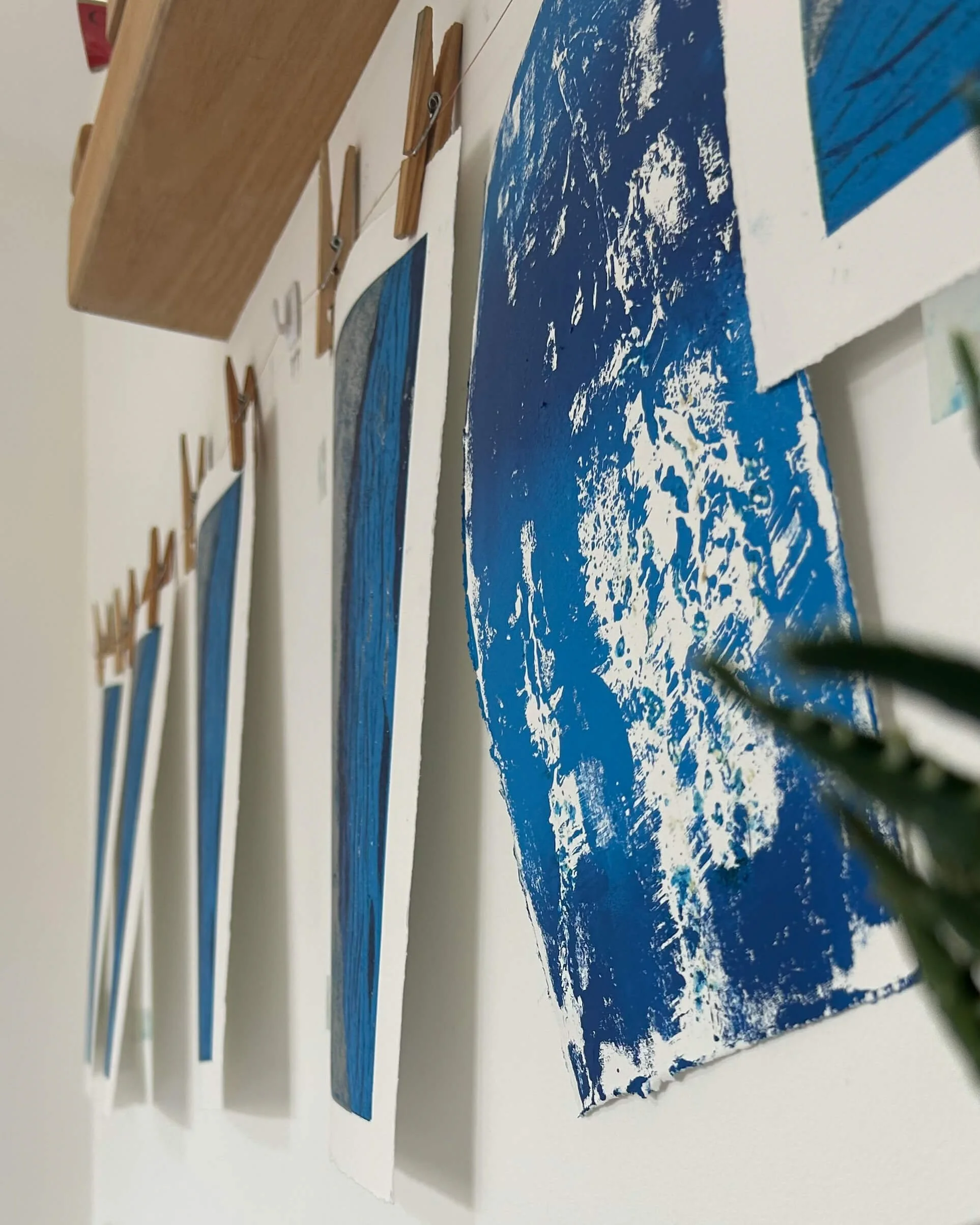 Studio shot of The Skipping Bridge drying on the peg wall - a lino reduction print of a silver grey stone bridge over a rippling blue river