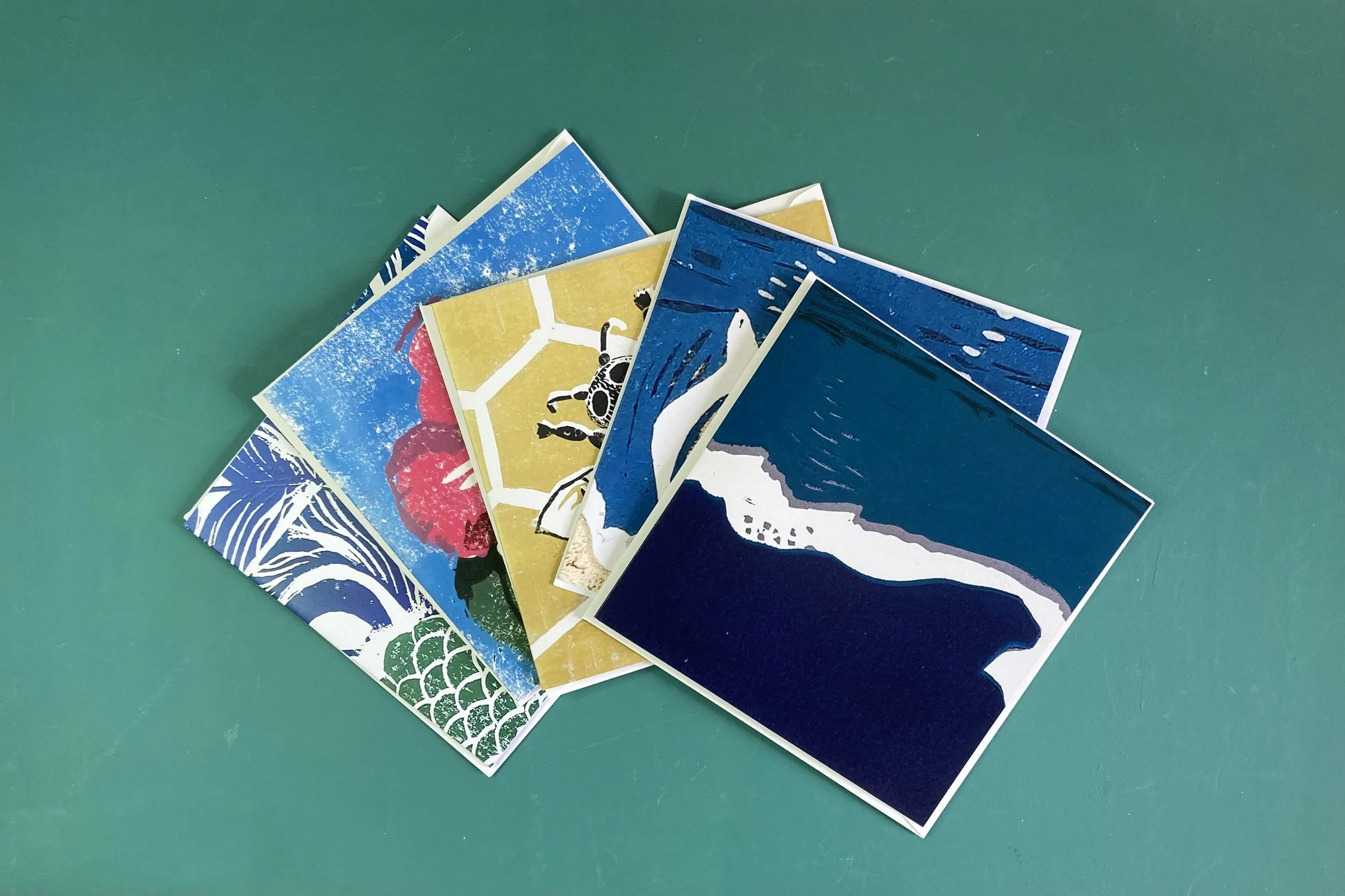 A collection of colorful postcards with various patterns and images, scattered on a teal surface.