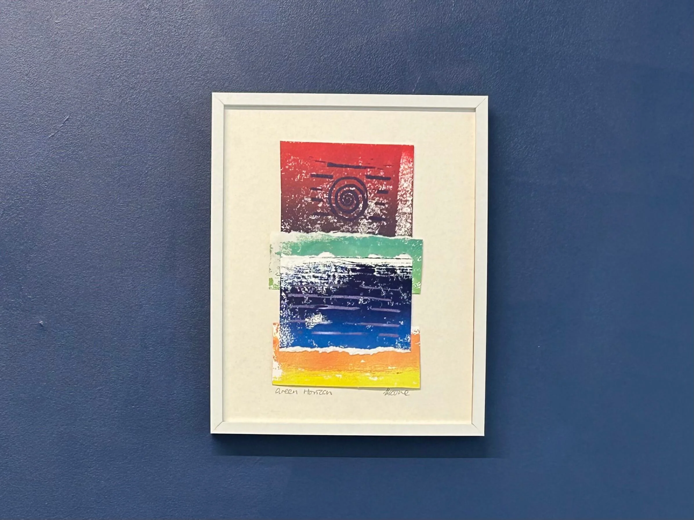 Blue green and pink mixed media collage and print in white frame on navy wall