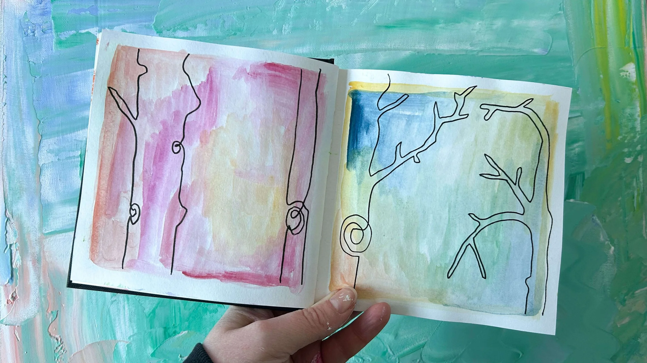 Heather Moore holding an open sketchbook showing black continuous line drawings of fantastical tree on colourful watercolour washes