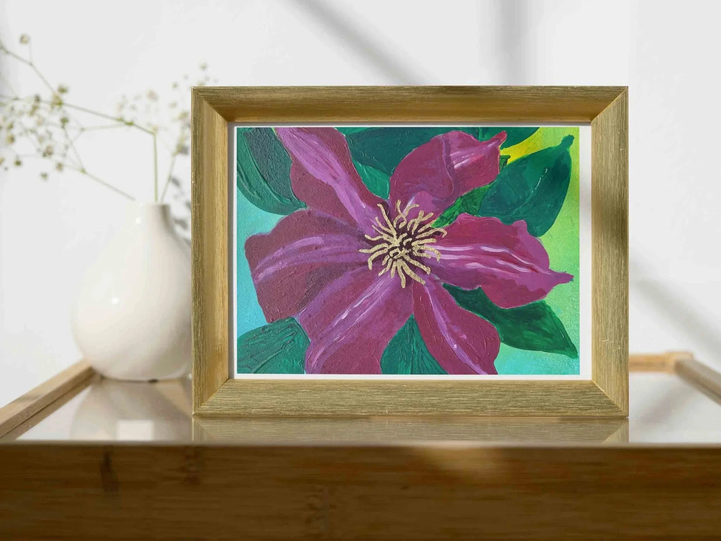 Postcard+of+burgundy+clematis+painting+in+a+small+gold+frame+atop+a+side+table+in+a+white+room+with+long+sgadows+on+the+wall.jpg