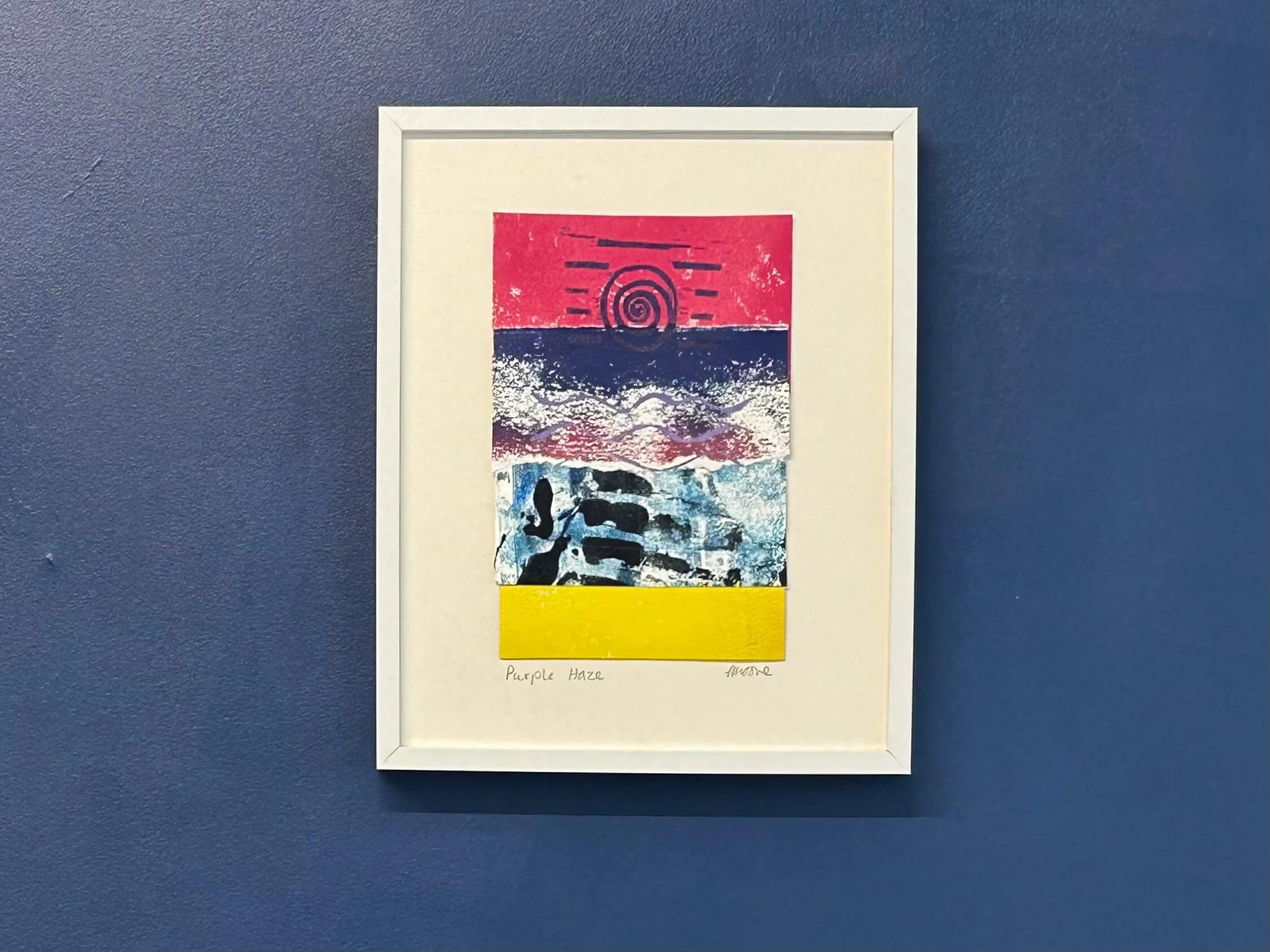 Pink blue and yellow mixed media collage and print in white frame on navy wall