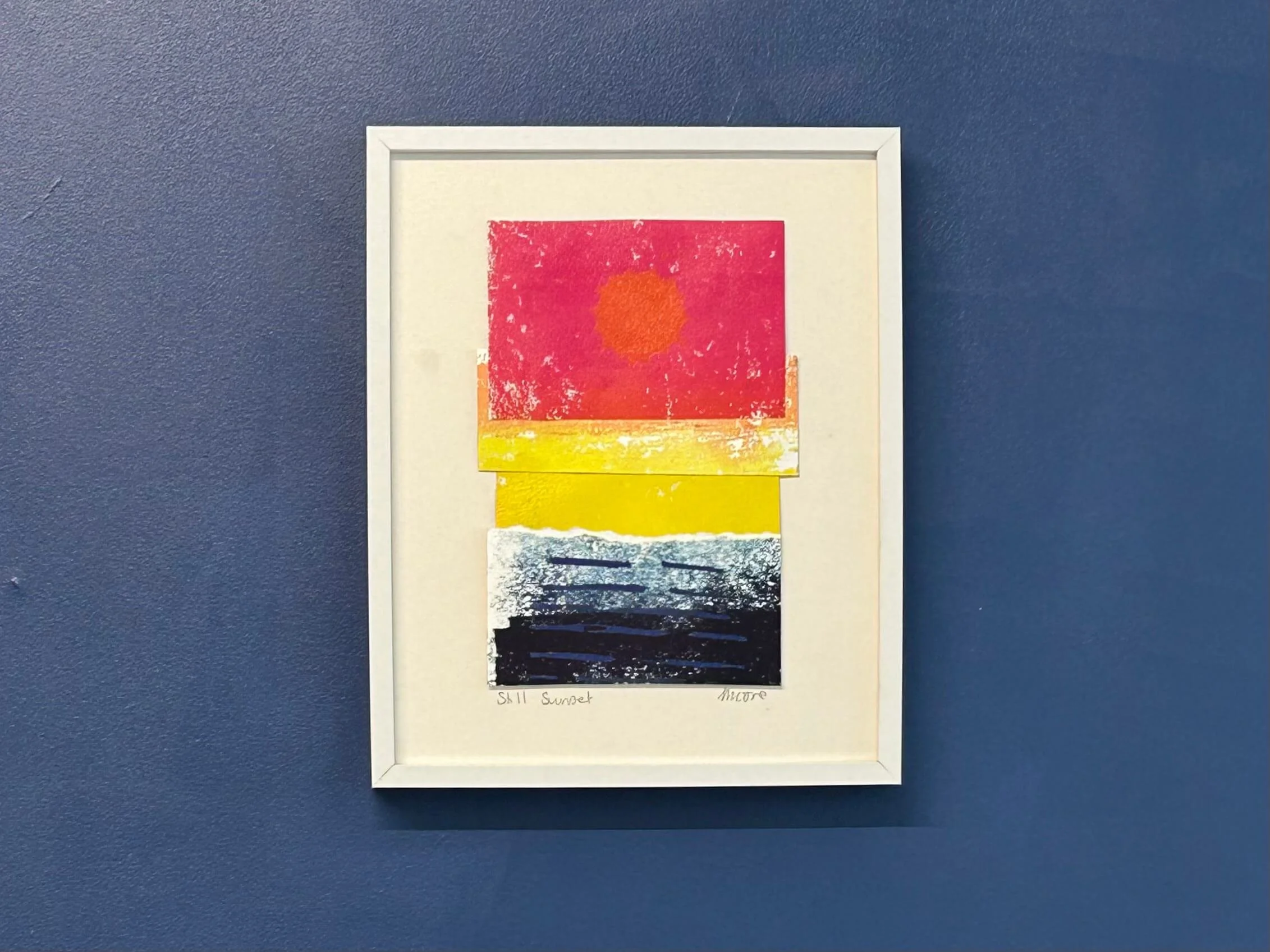 Pink yellow and blue mixed media collage and print in white frame on navy wall