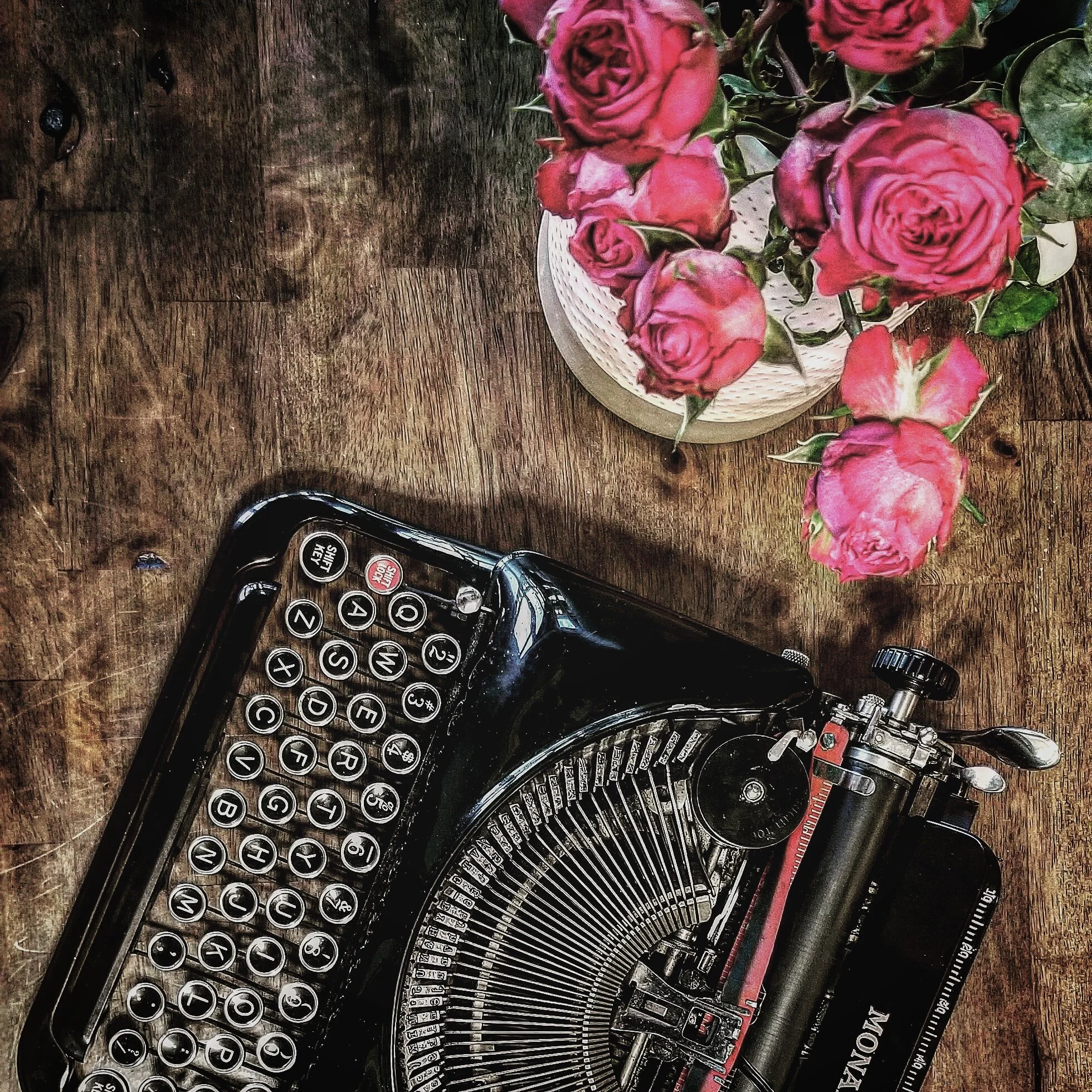 Restored Remington Model 5 Streamliner typewriter in gloss black, on weathered wood with pink roses.