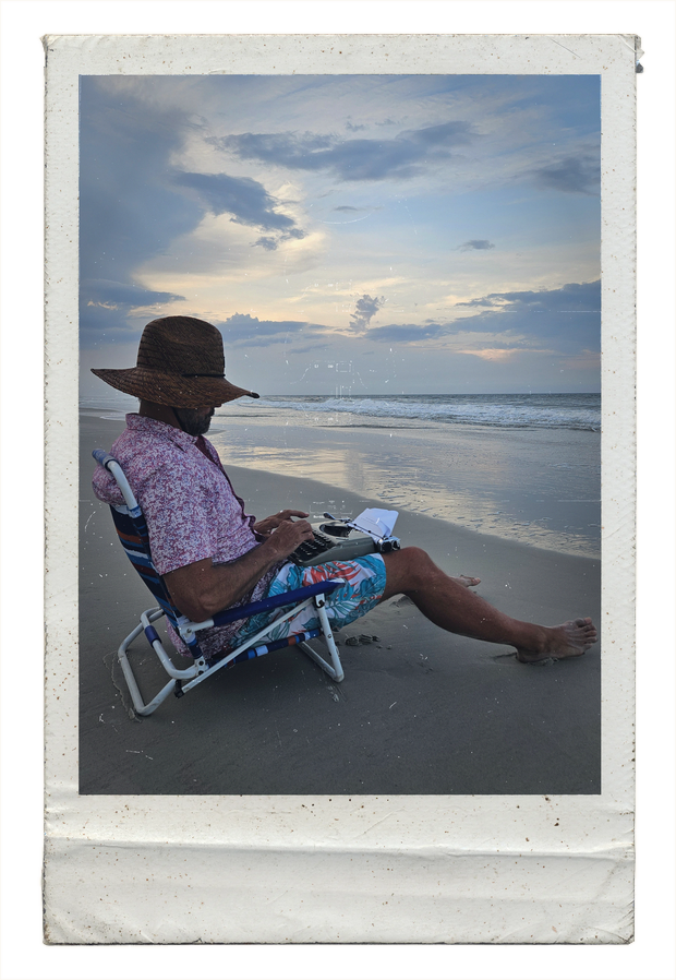 Steven Budden typing on the beach on a Groma Kolibri typewriter.