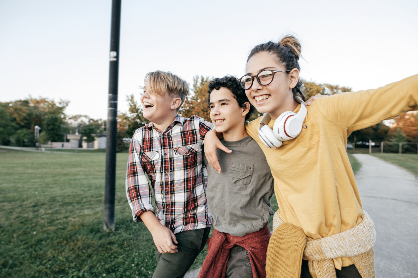 Three children walking outdoors in a park, smiling and enjoying each other's company.