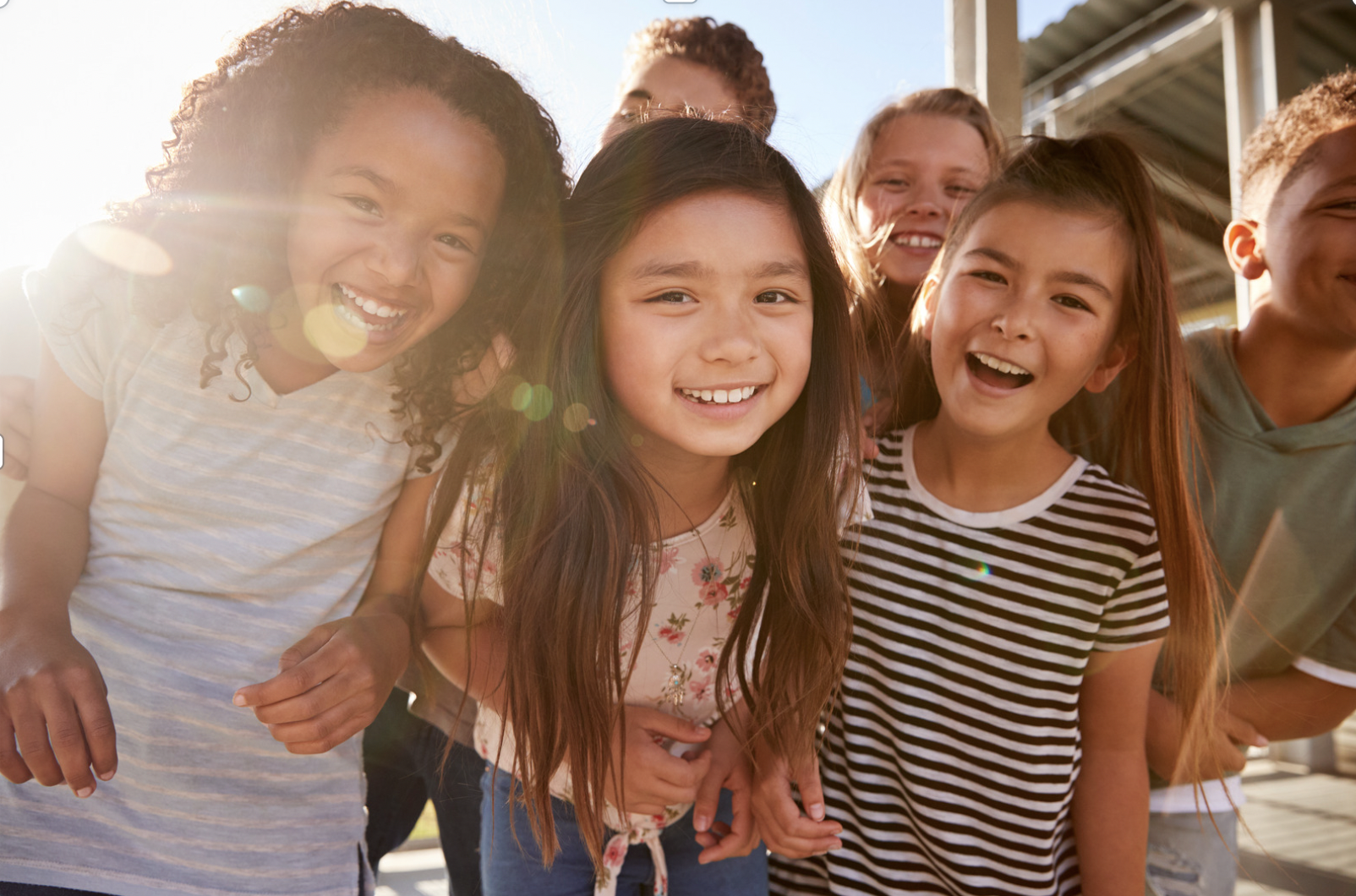 Group of children smiling and laughing outdoors in sunlight.