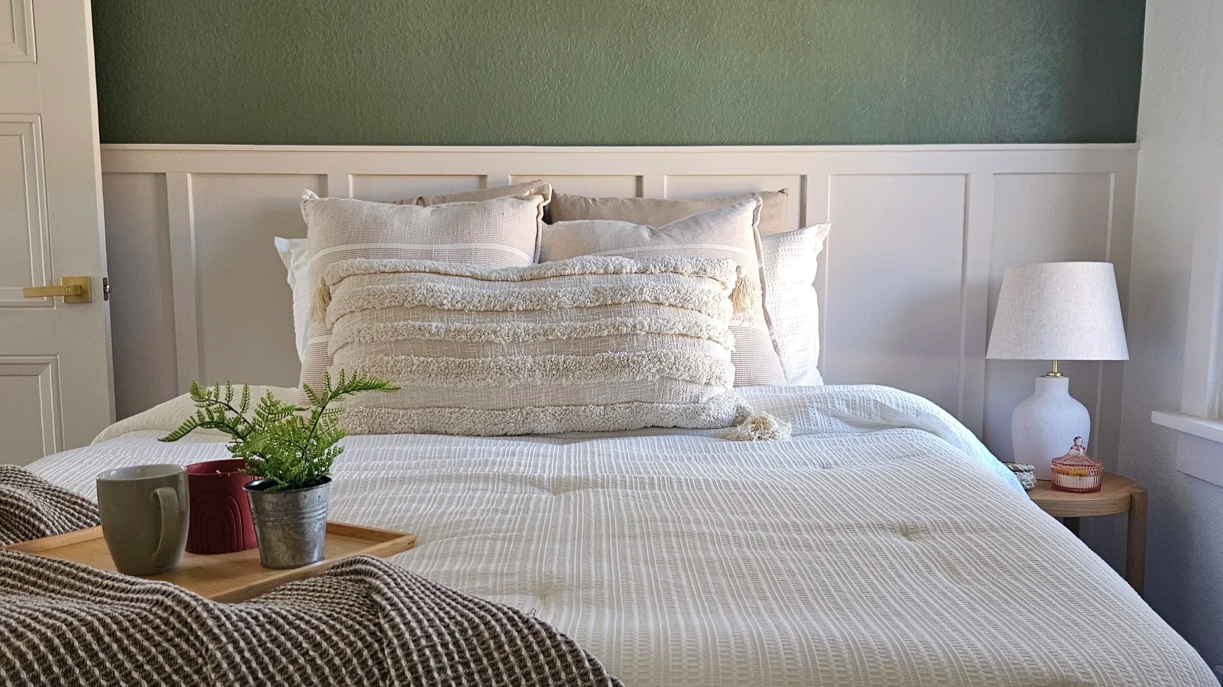 A bedroom with white linens & a wooden tray with a mug and vases.