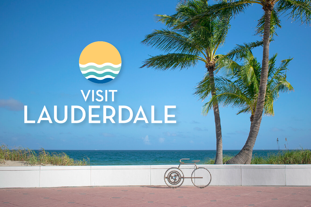 Souvenir sign encouraging visitors to come to Lauderdale with palm trees, a bicycle, and the ocean in the background.