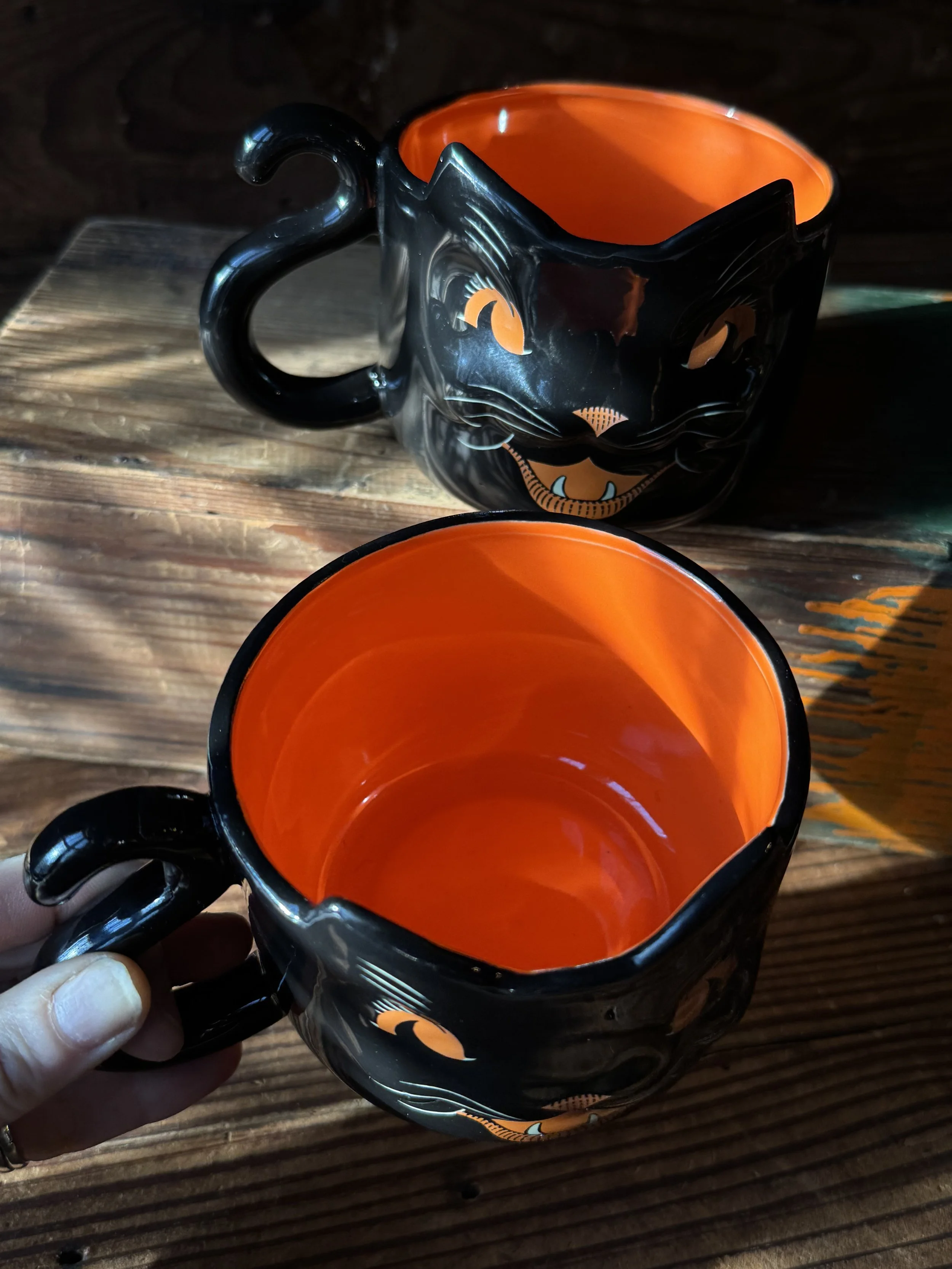 a vintage style black cat mug with a curling tail handle and a bright orange inside