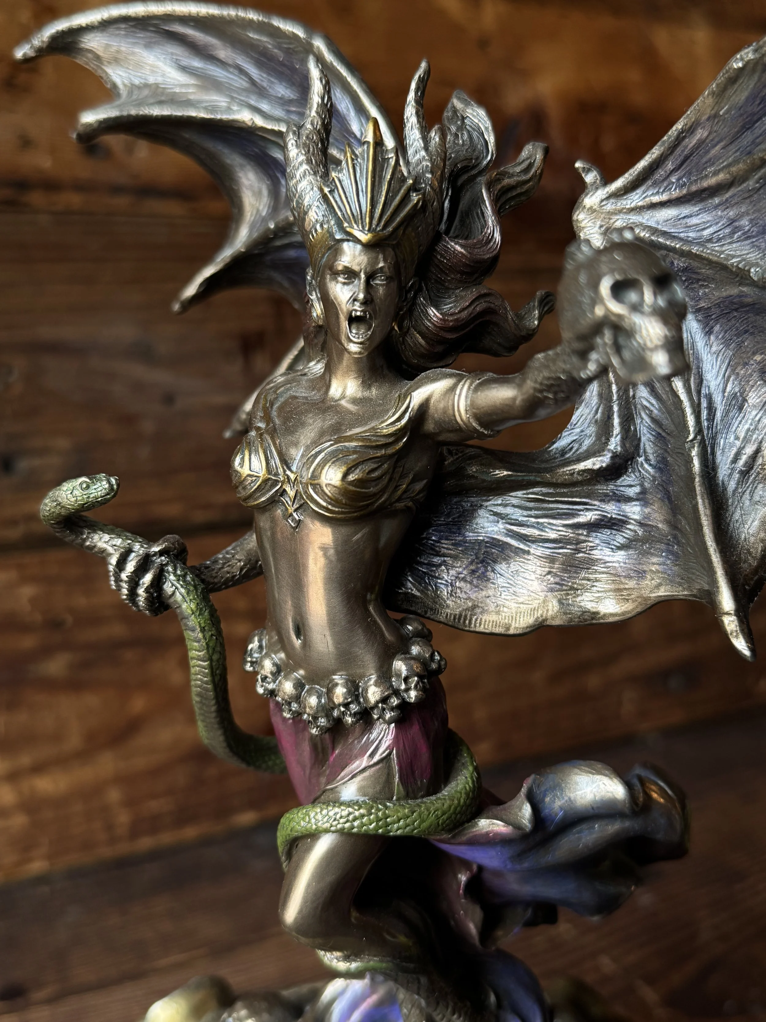 A bronze, purple, and green resin statue of the goddess Lilith with snake and skull in her hand.