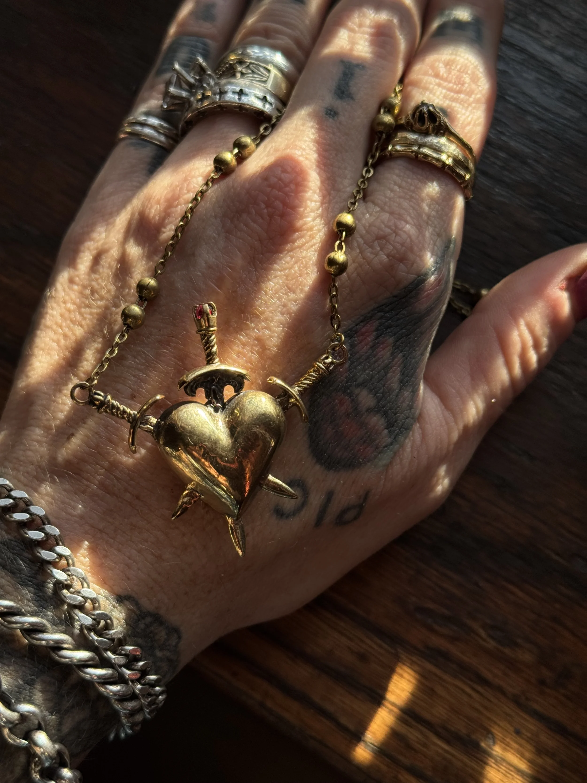 brass three of swords necklace by ozma adornments with a garnet stone and a triple pierced heart on one side and a hand carved naked lady on the other