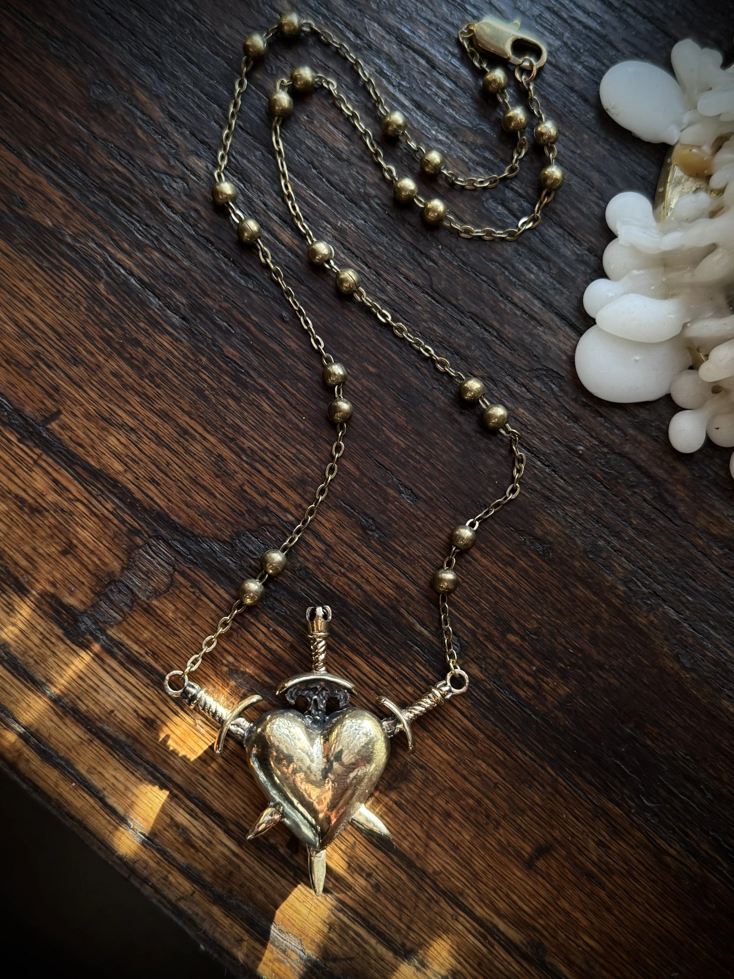 brass three of swords necklace by ozma adornments with a garnet stone and a triple pierced heart on one side and a hand carved naked lady on the other