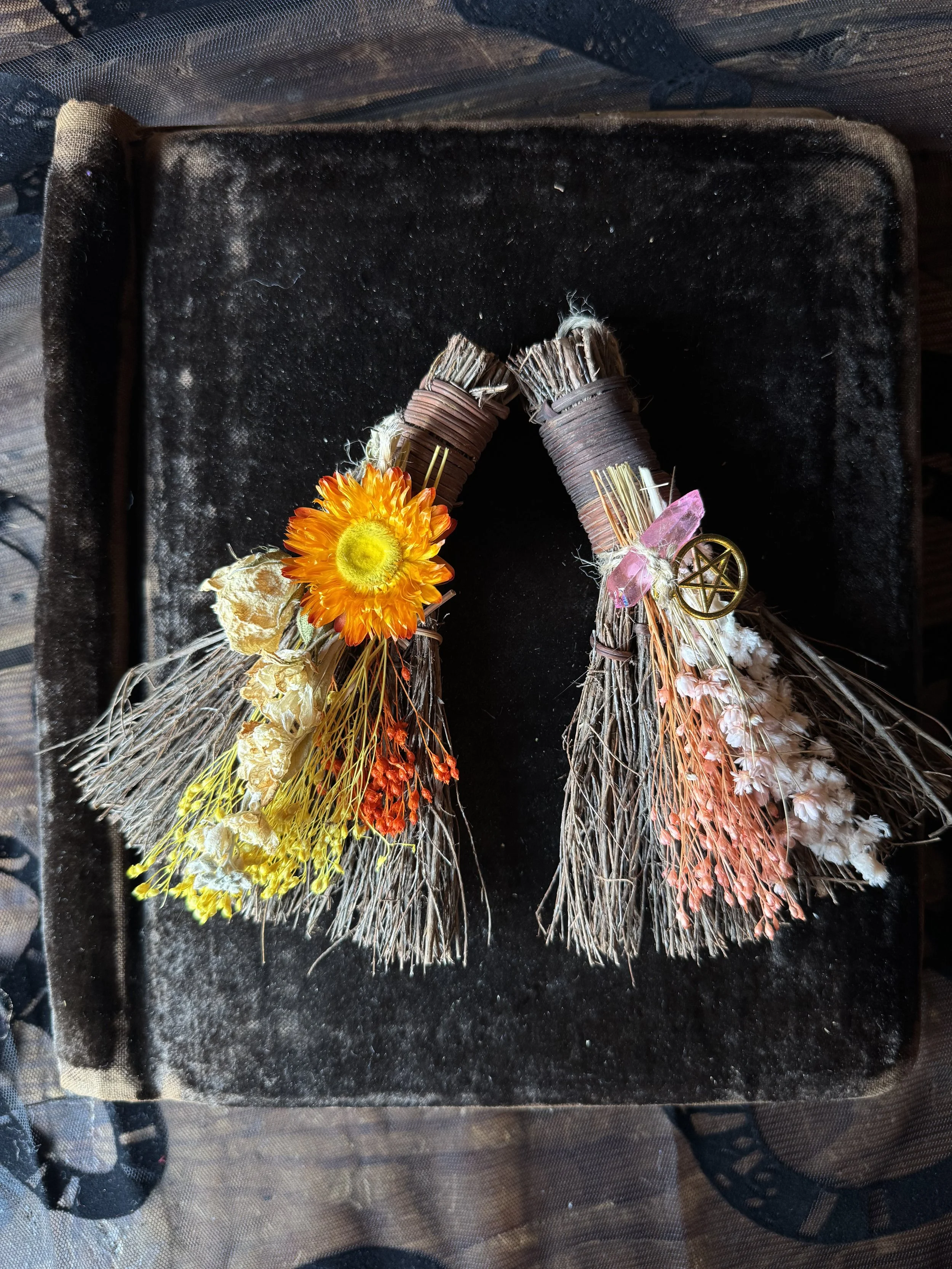 Handmade magical brooms dressed with flowers, talismans, and crystals.