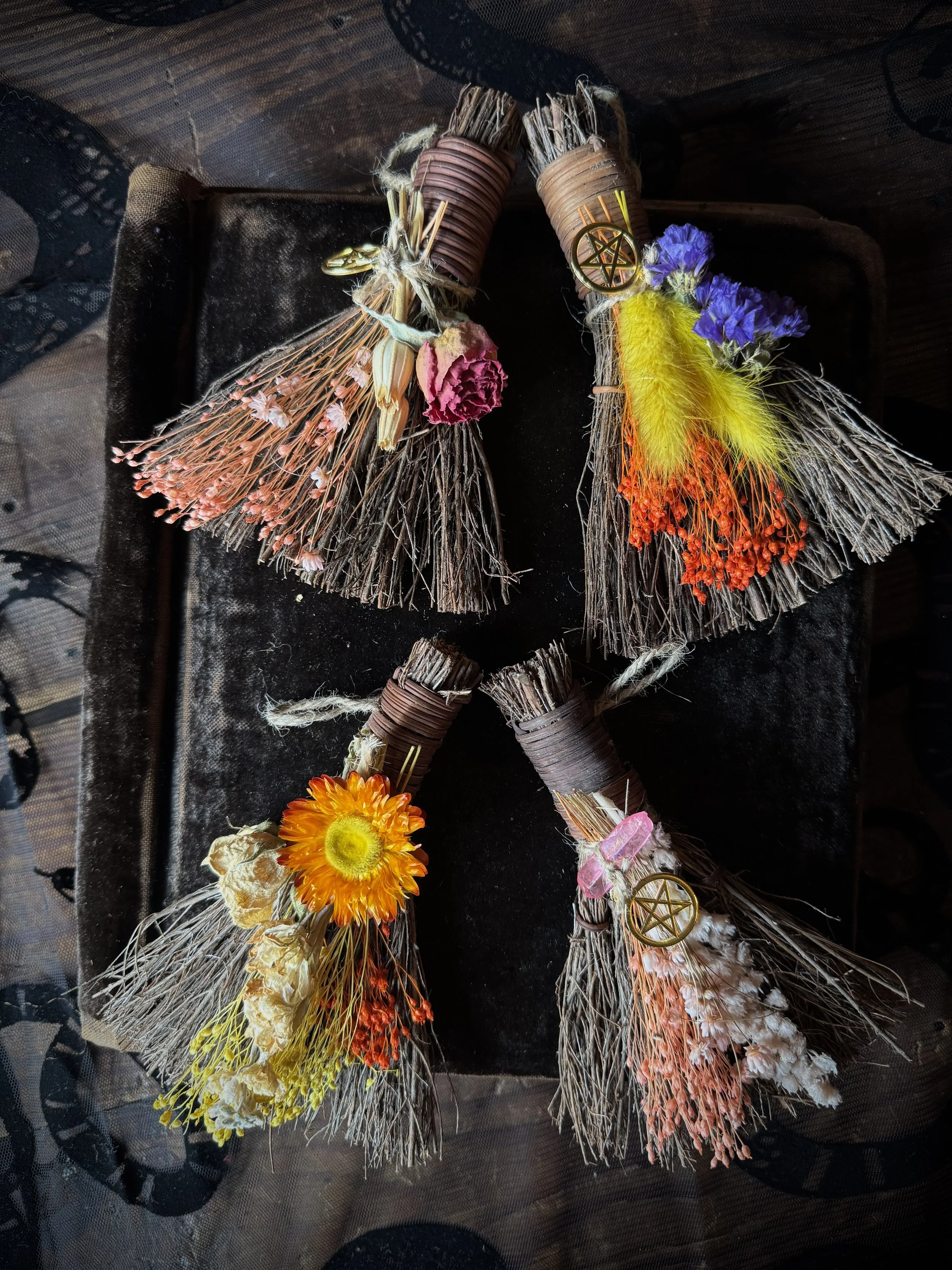 Handmade magical brooms dressed with flowers, talismans, and crystals.