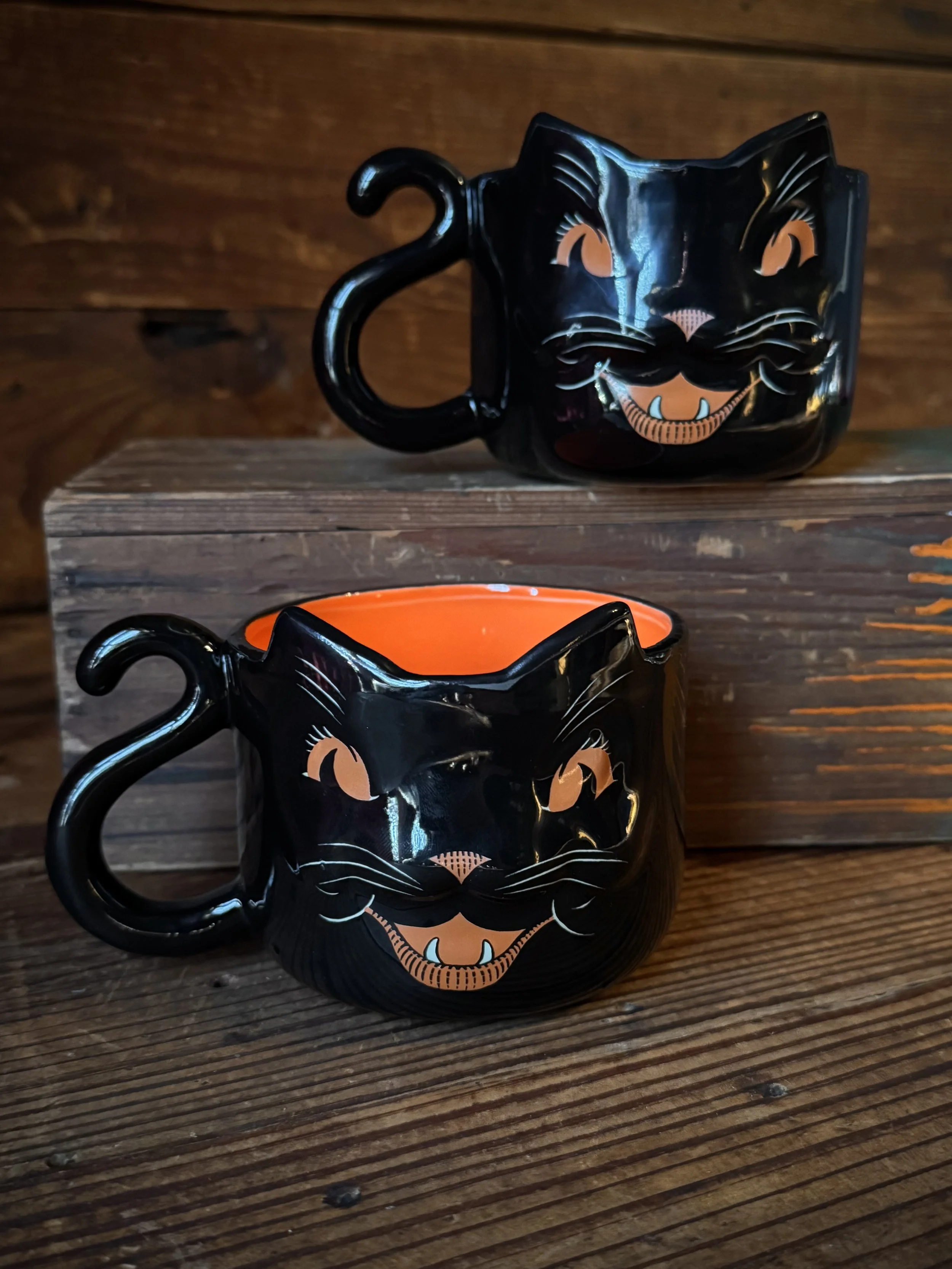 a vintage style black cat mug with a curling tail handle and a bright orange inside