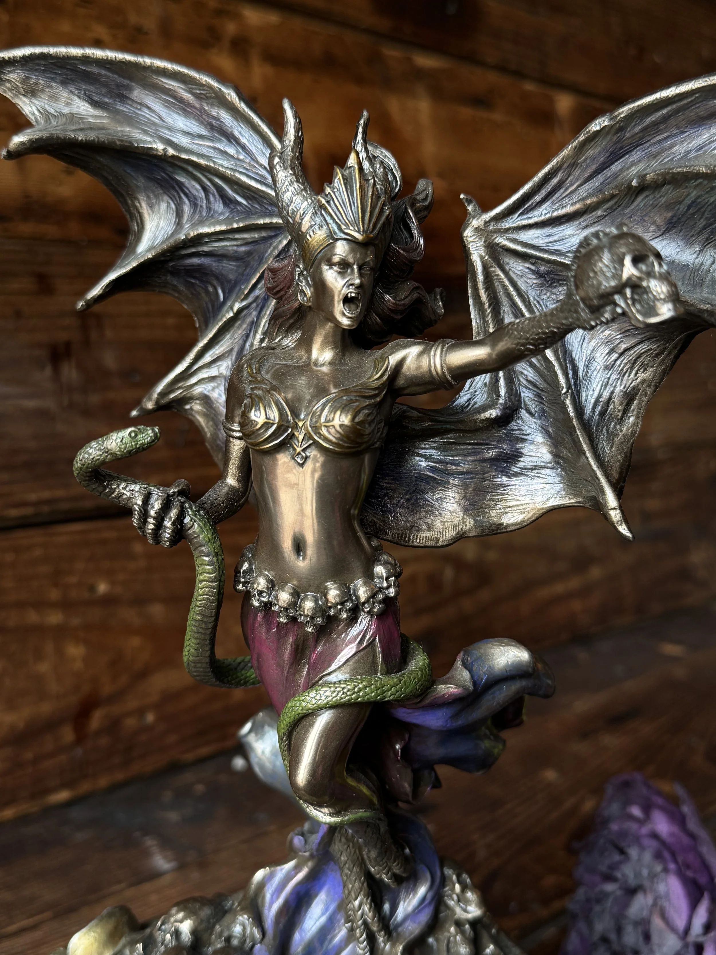 A bronze, purple, and green resin statue of the goddess Lilith with snake and skull in her hand.