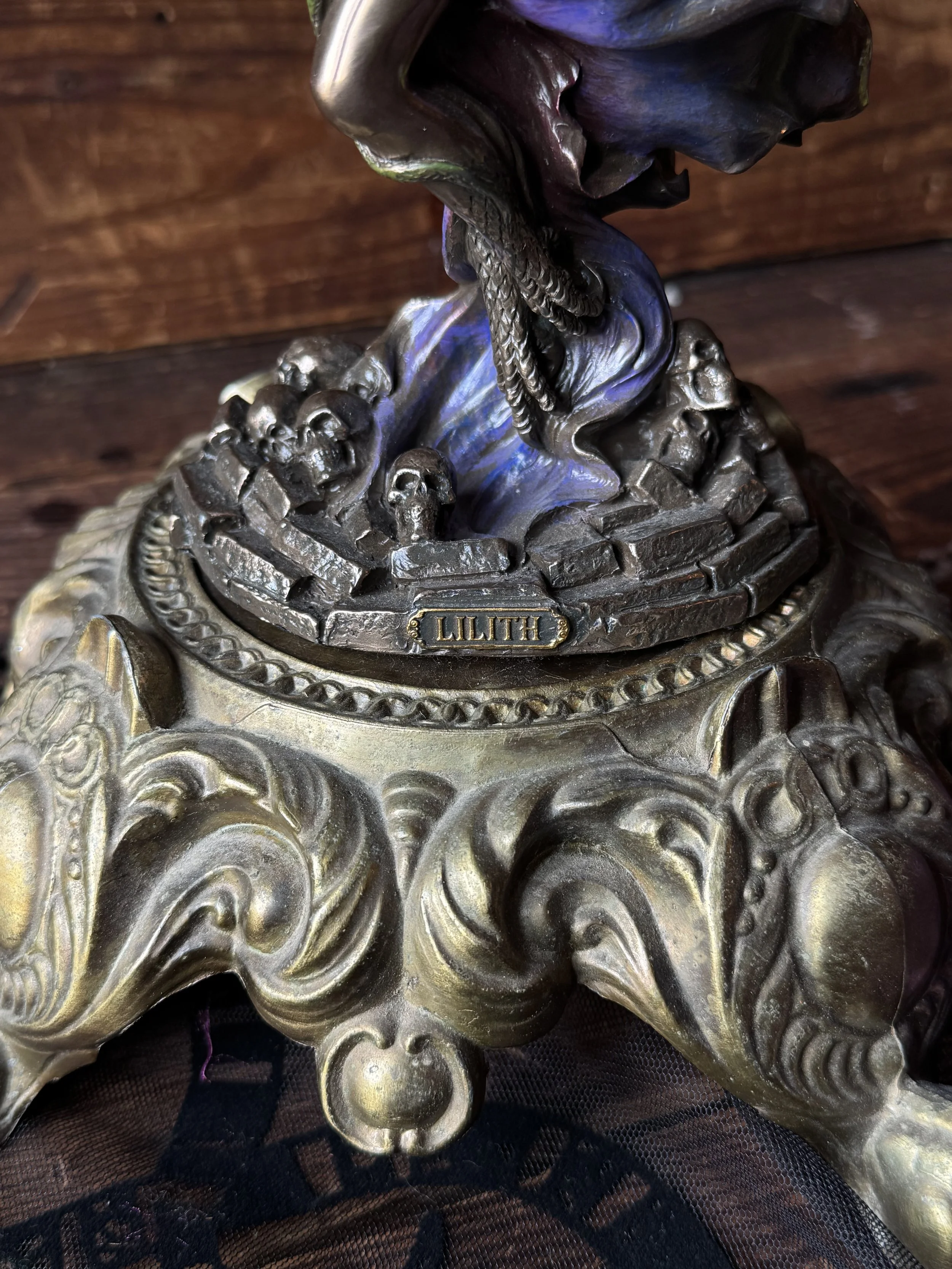 A bronze, purple, and green resin statue of the goddess Lilith with snake and skull in her hand.