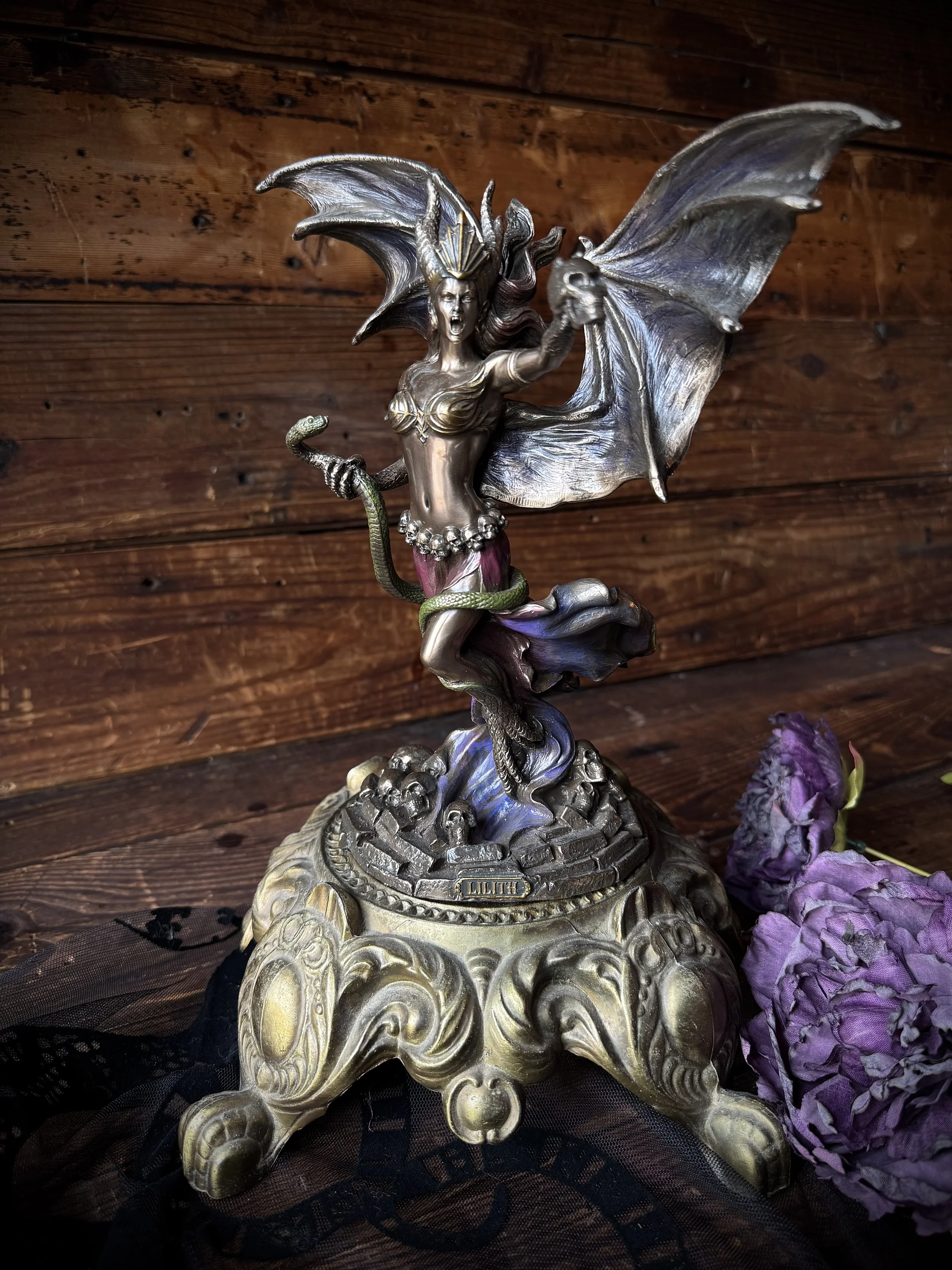 A bronze, purple, and green resin statue of the goddess Lilith with snake and skull in her hand.
