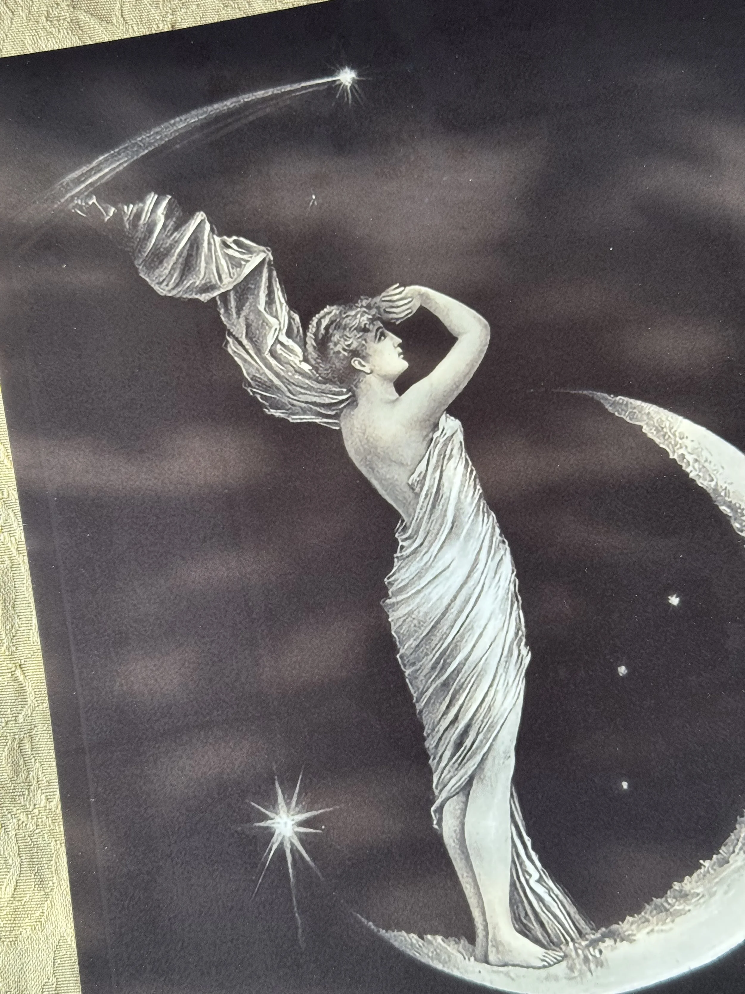a black and white print with a grecian, cloaked woman standing atop a crescent moon