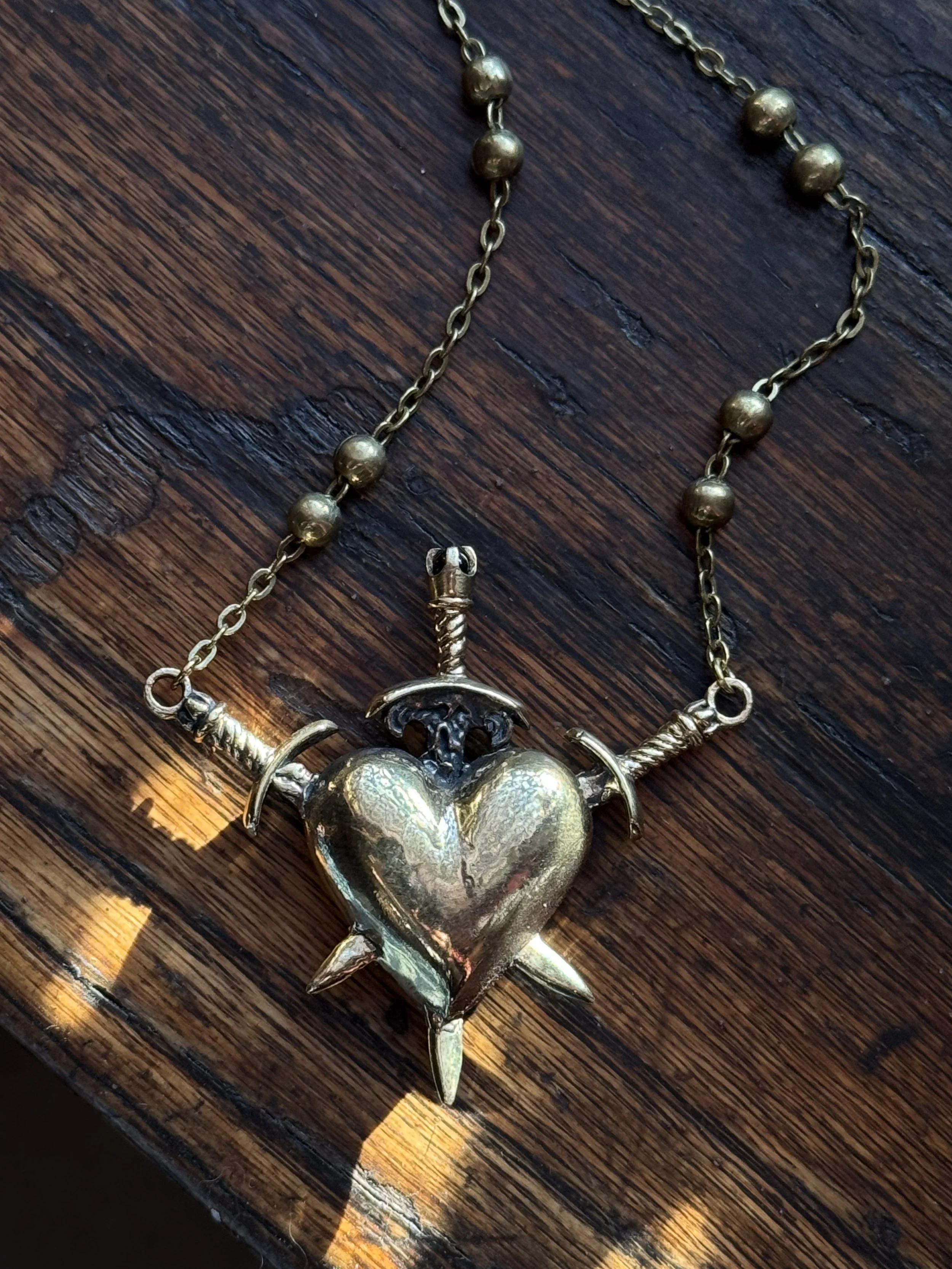 brass three of swords necklace by ozma adornments with a garnet stone and a triple pierced heart on one side and a hand carved naked lady on the other