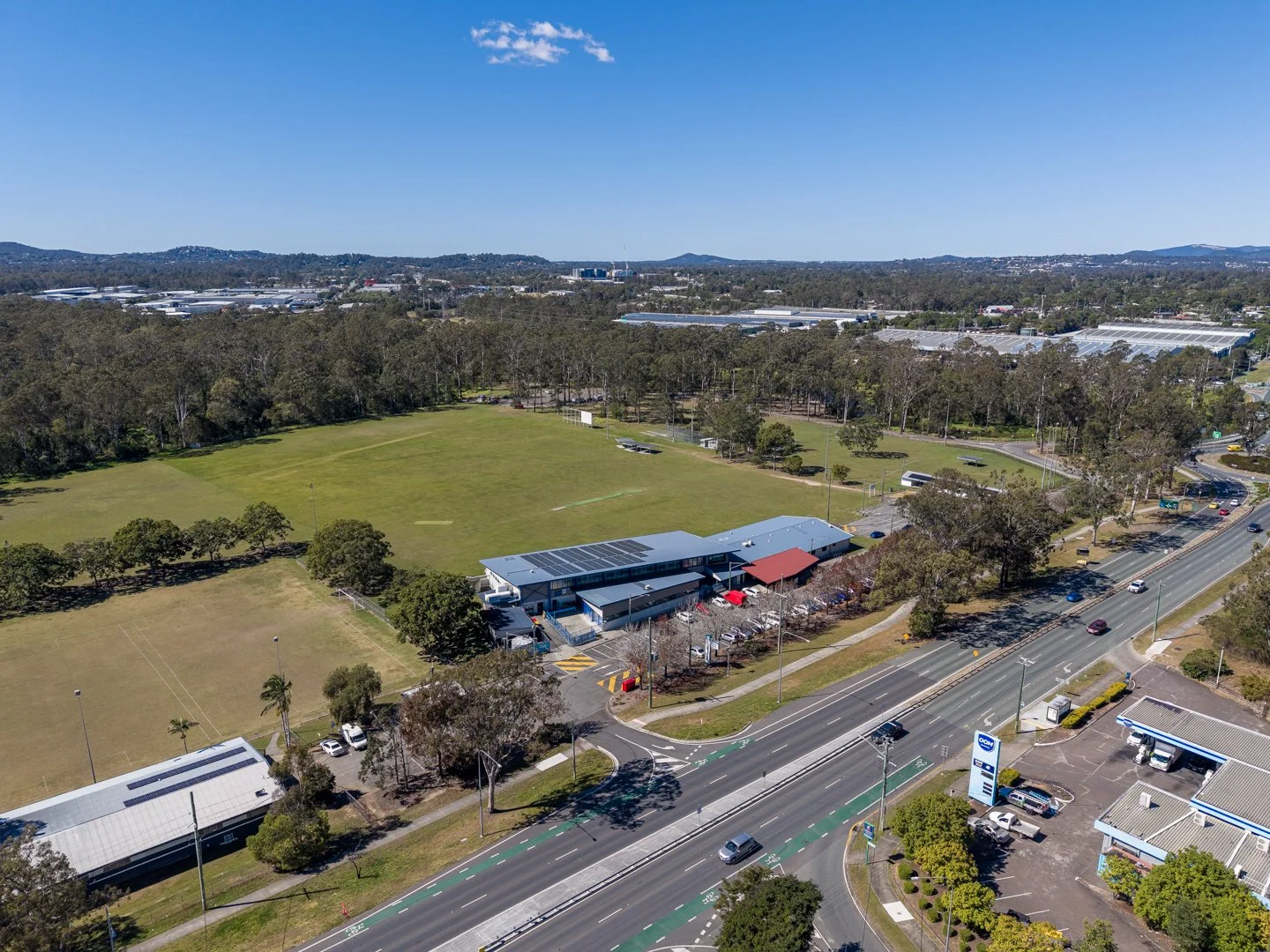 Aerial view of a sports oval and clubhouse in Kingston QLD, with the Logan Motorway industrial corridor visible in the background.