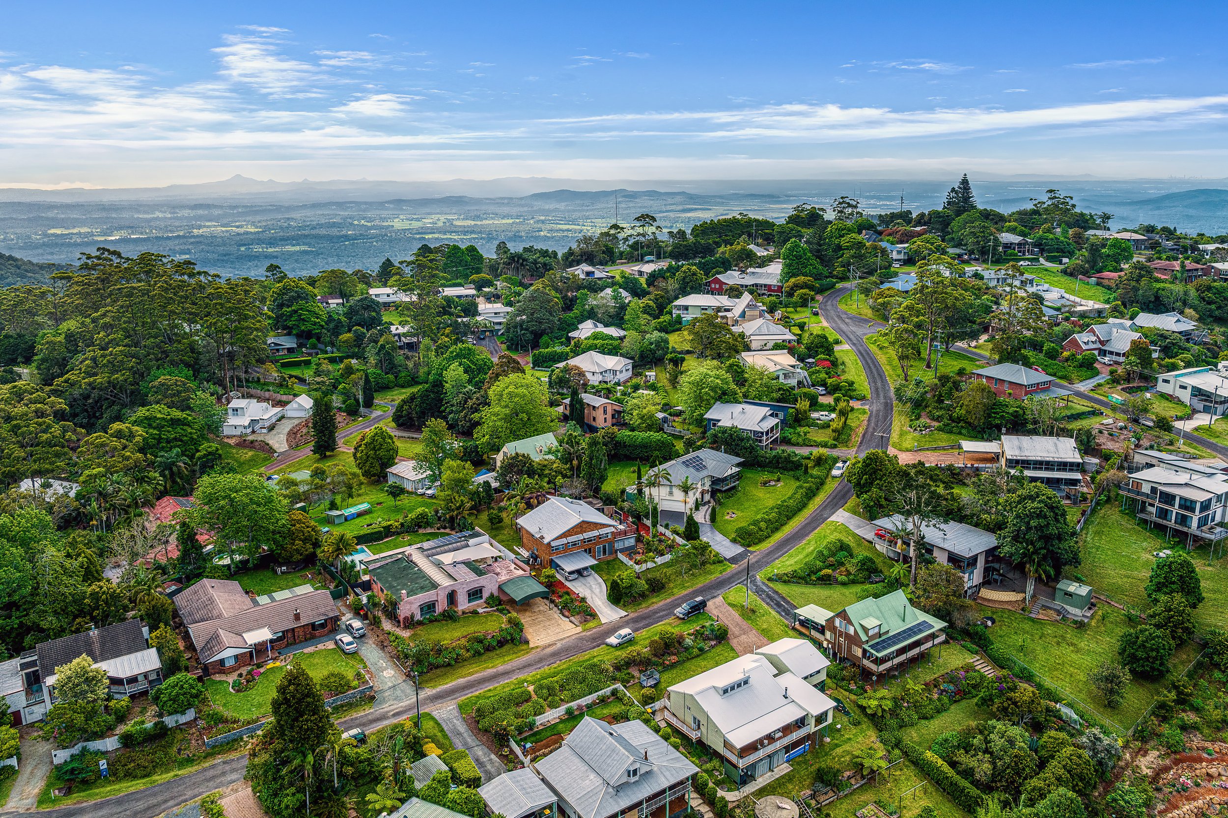  Aerial view of residential suburb showing rooftops, tree canopy and ocean horizon — drone photography SEQ Digital 1 QLD 