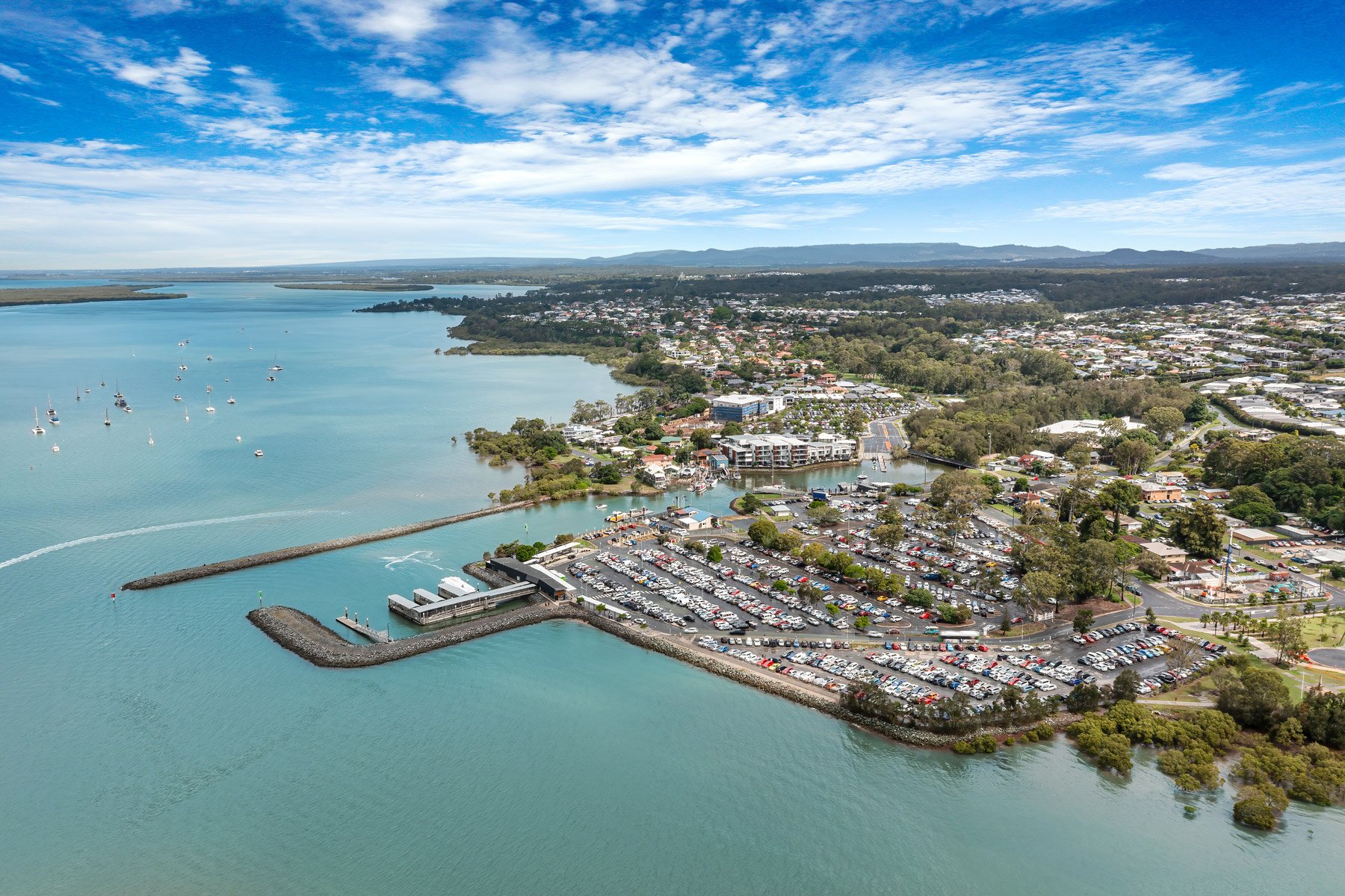 Coastal aerial view of Redland Bay, Queensland, featuring the ferry terminal, calm ocean waters, and waterfront community.