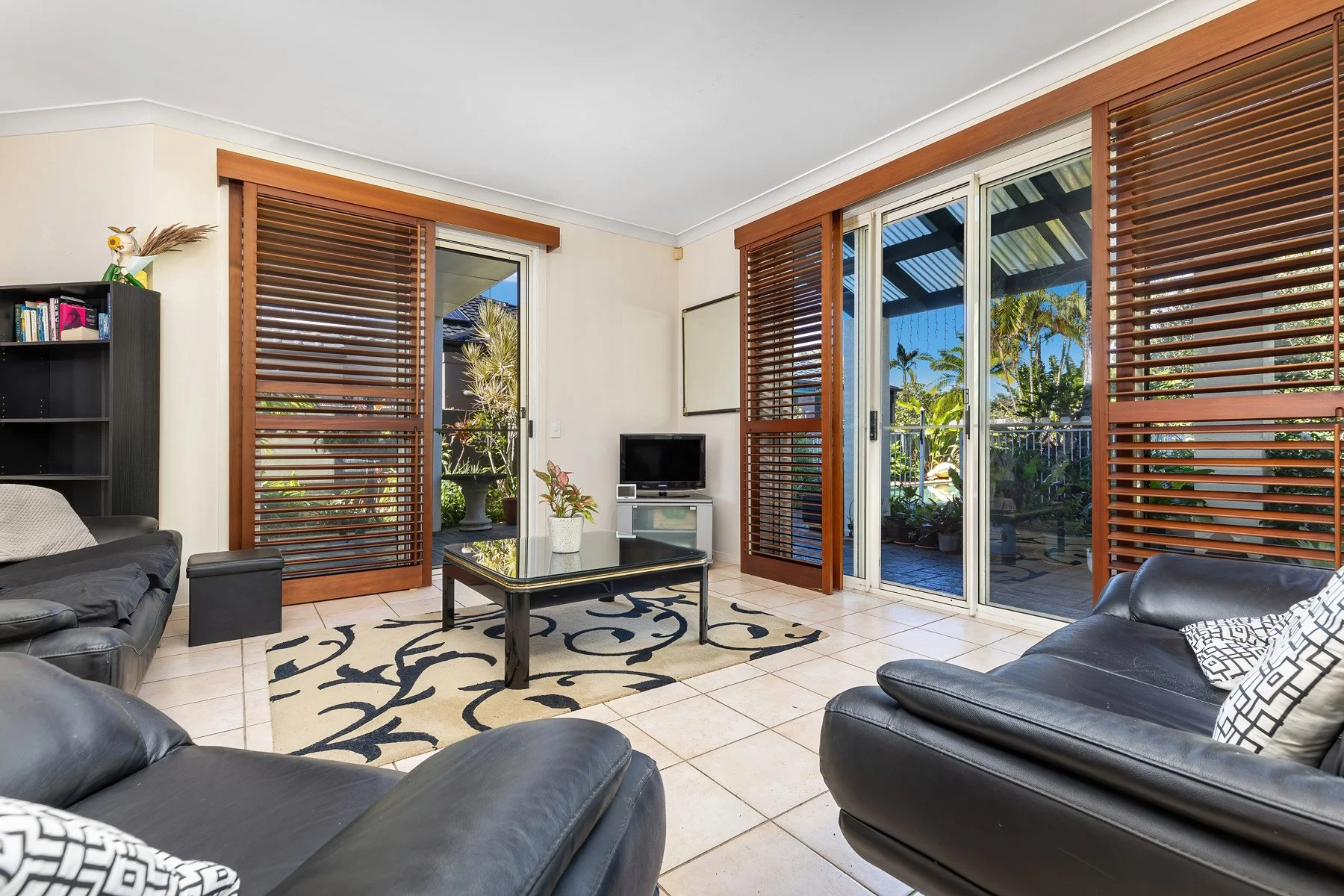 Bright open-plan living room in a modern Springwood home, featuring white tiled floors, plantation shutters, and an indoor-outdoor flow to the backyard.