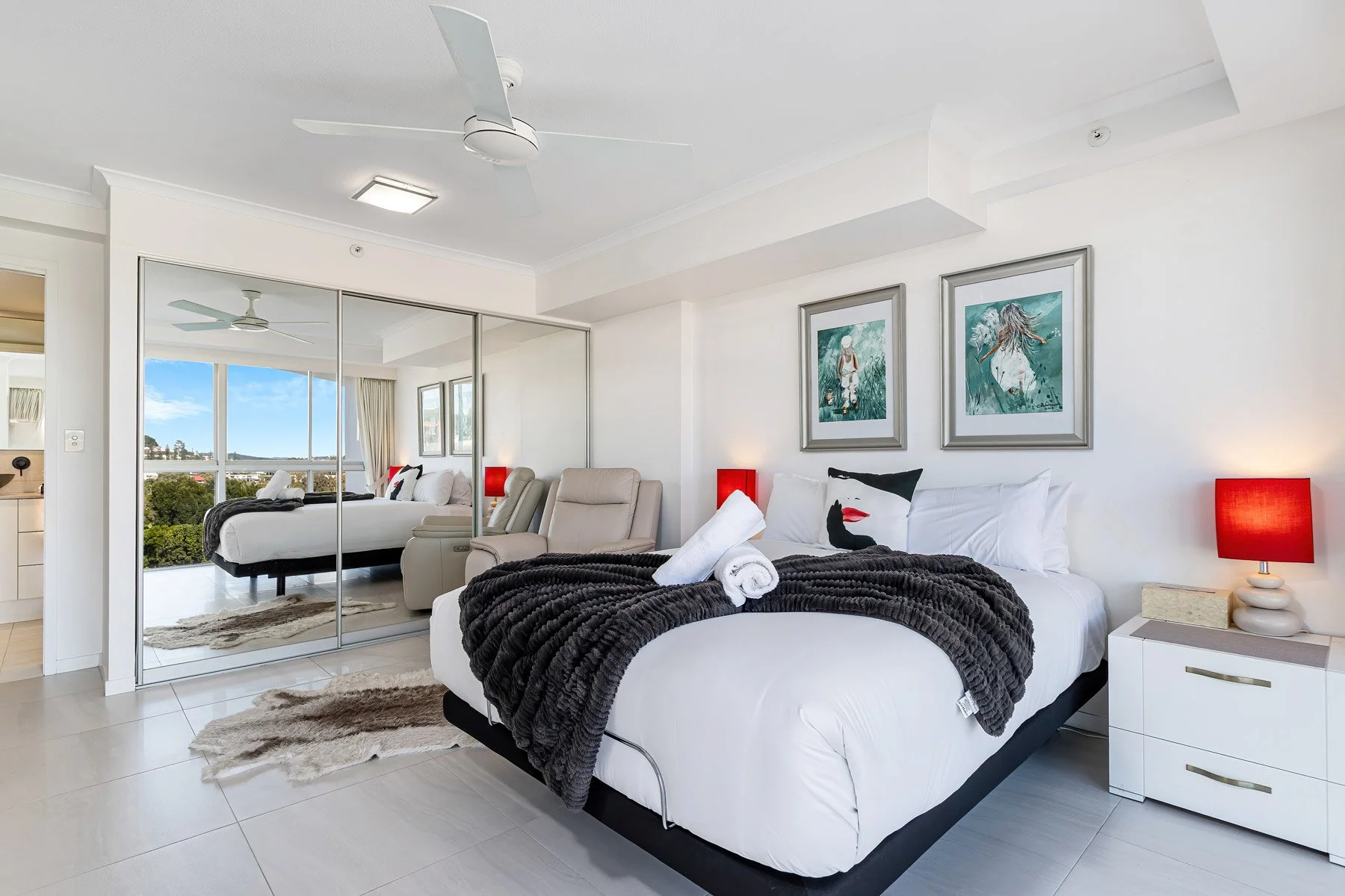 Bright Airbnb bedroom in Coolangatta, Gold Coast, featuring a styled queen bed, mirrored wardrobe reflecting the sky, and coastal decor.