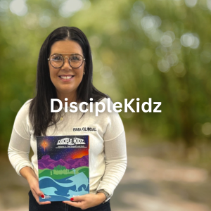 Young woman holding a book outdoors, smiling, wearing glasses and a white shirt, with a blurred green background.