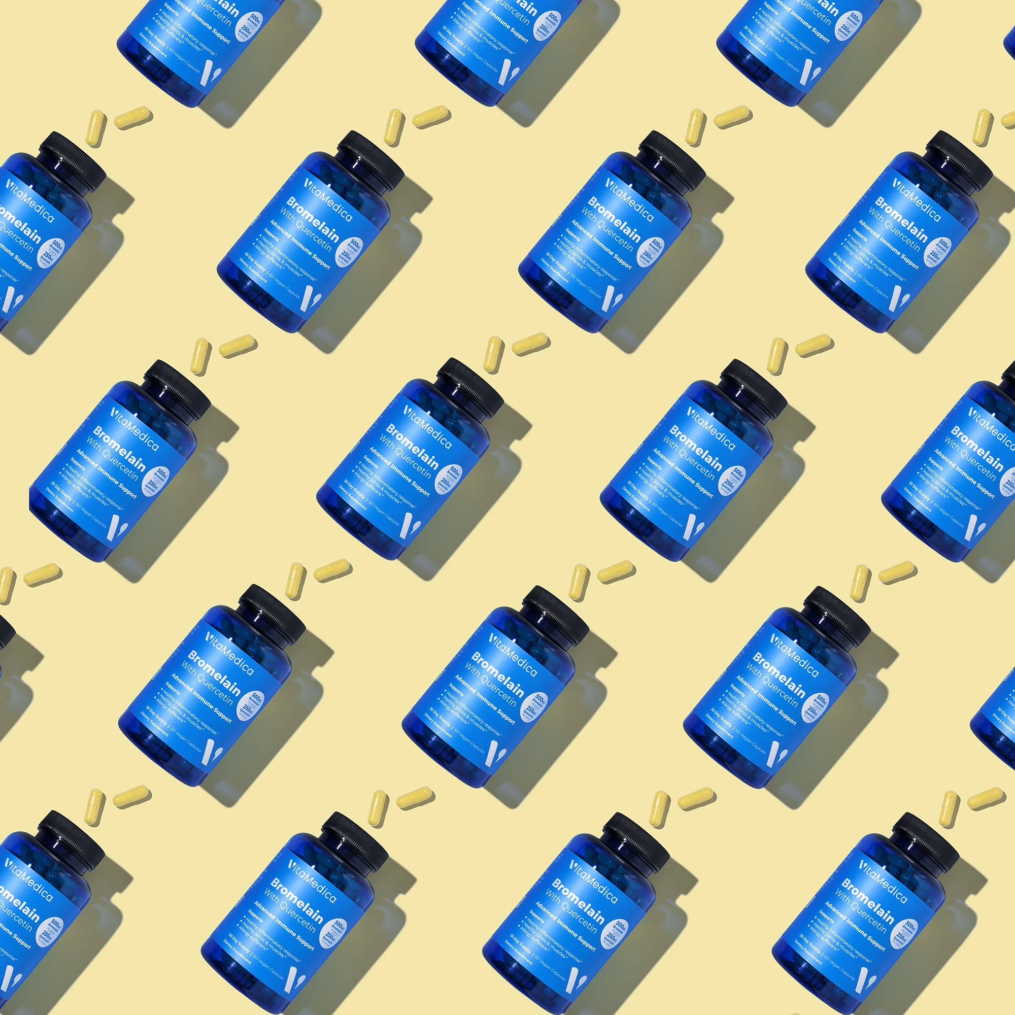 Multiple bottles of blue-colored dietary supplement labeled 'VitaMedica Bromelain with Quercetin' on a yellow background, with yellow capsules scattered around.