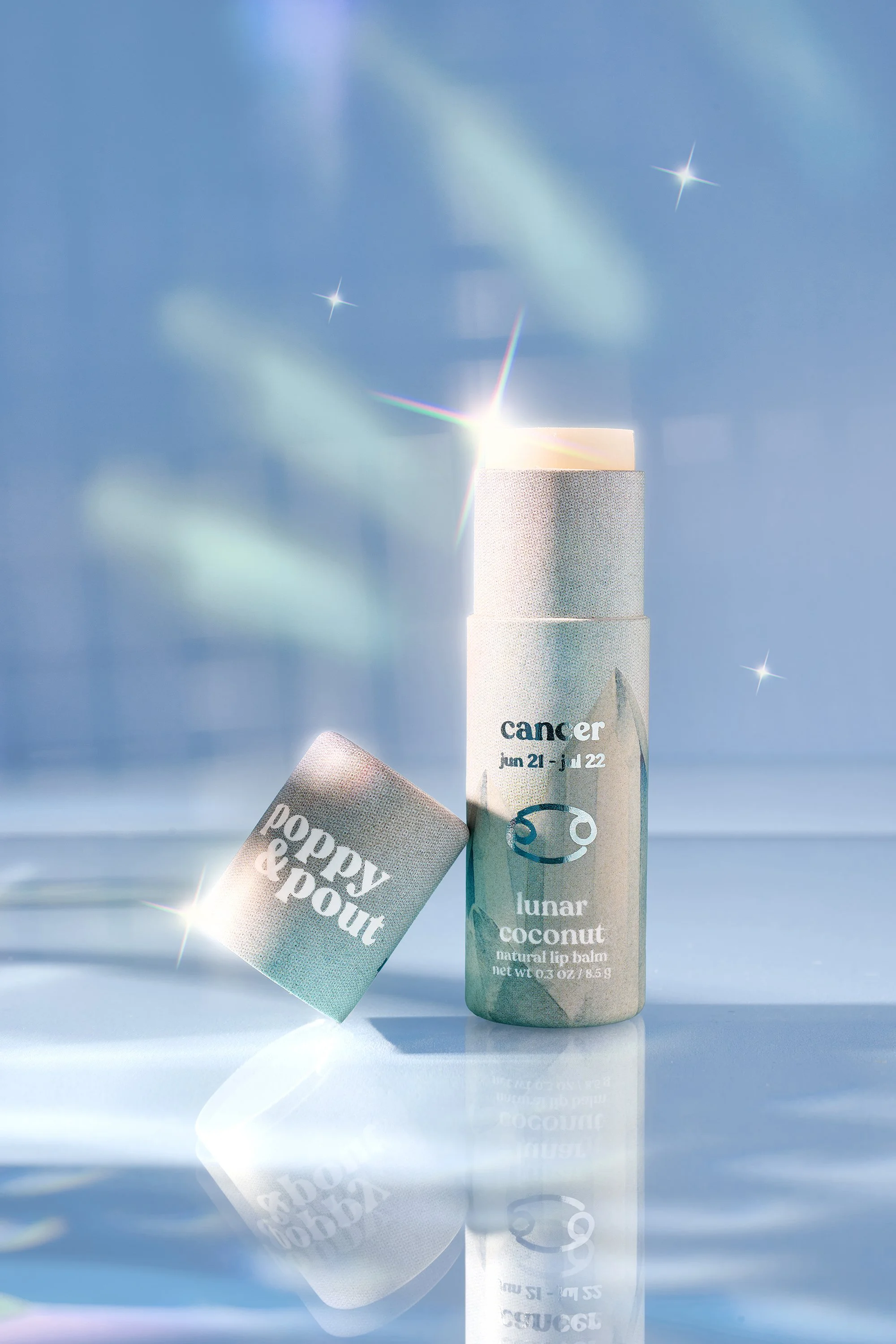 Poppy and Pout Lip balm tube labeled 'lunar coconut' with light reflections and a blue starry background.