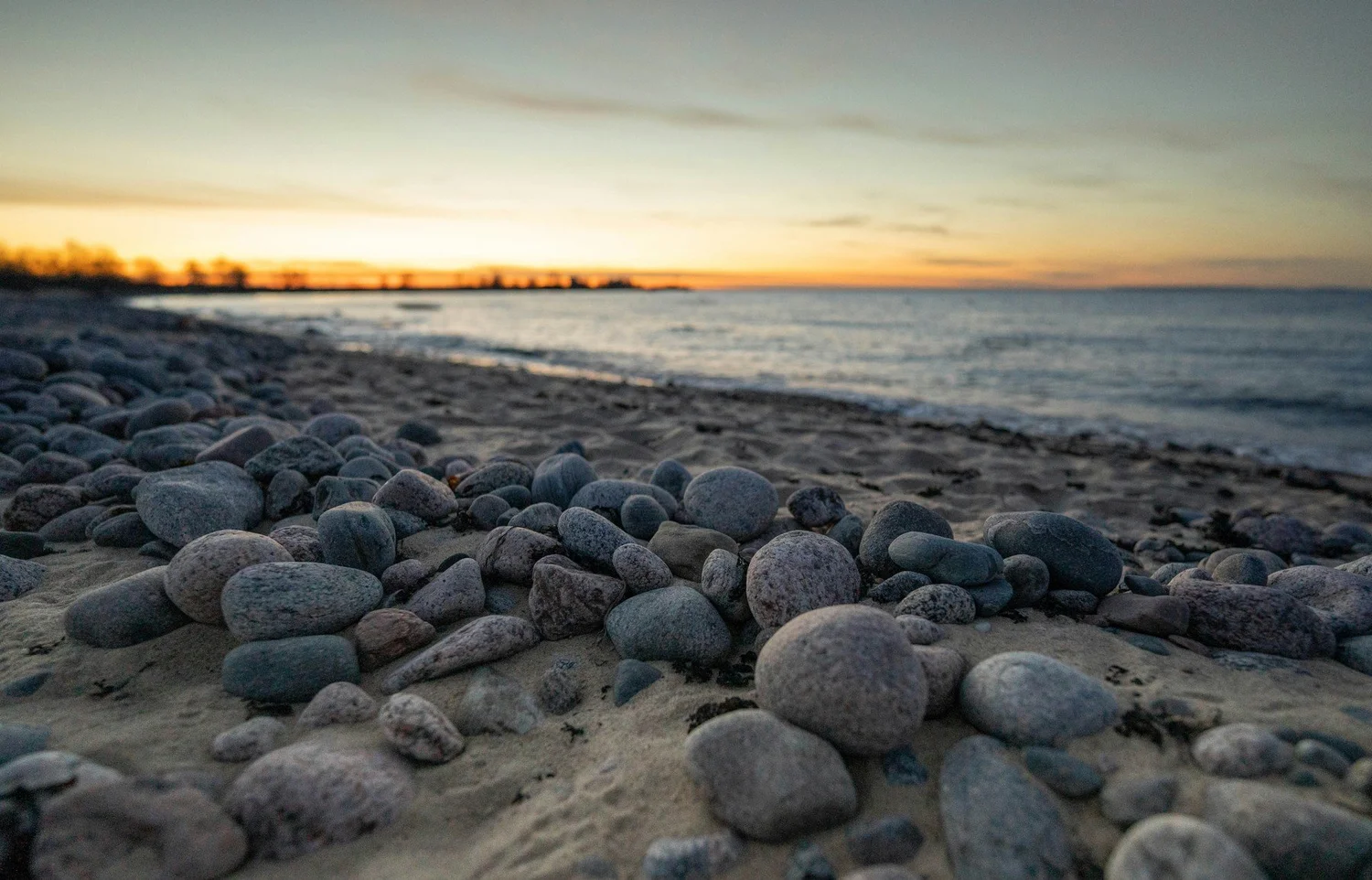 Smooth pebbles beside calm water under a soft sunset sky.