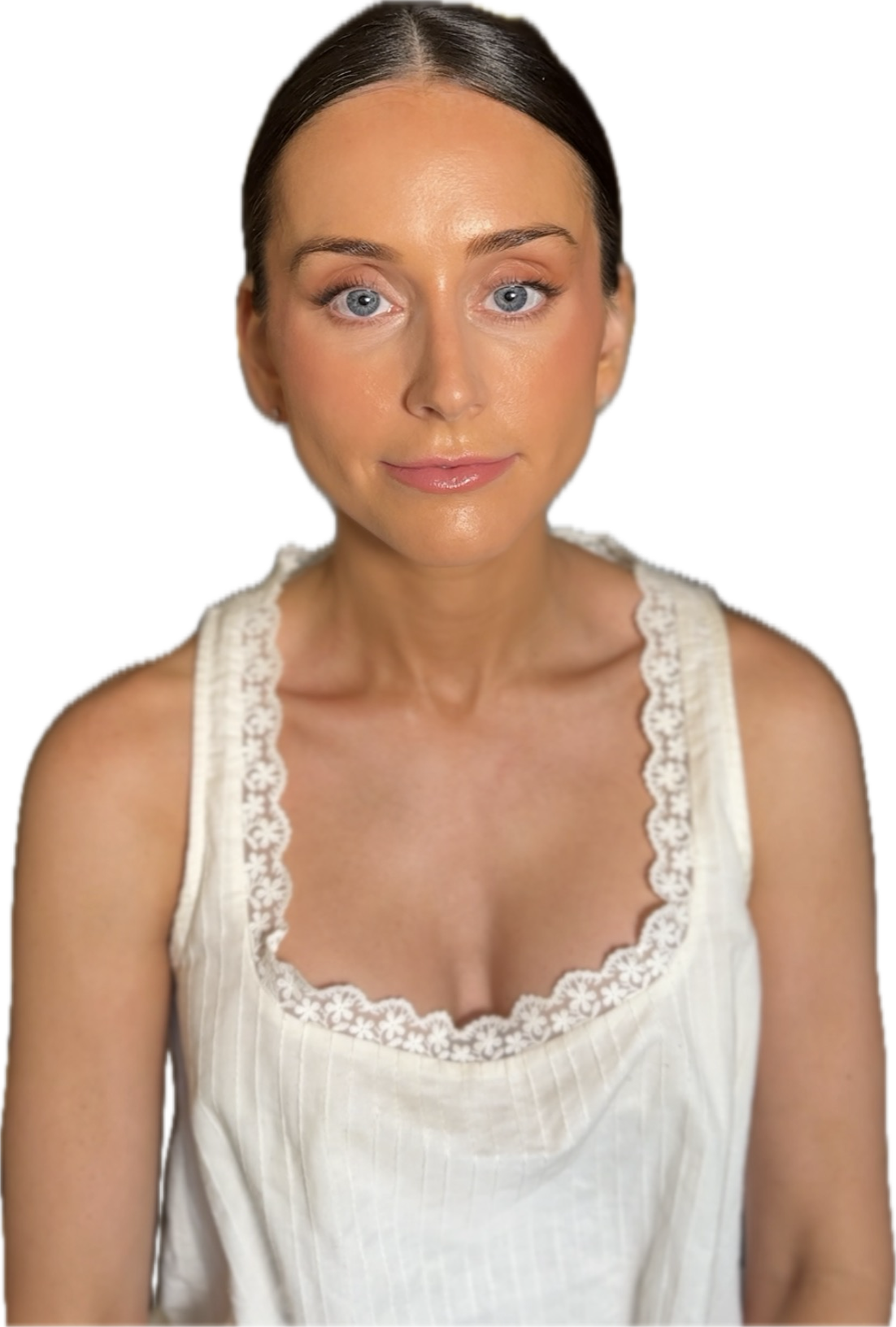 A woman with blue eyes and dark brown hair wearing a sleeveless white top with lace edges, sitting indoors.