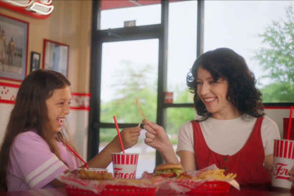 A woman and a girl laughing and sharing a fry inside a fast food restaurant.