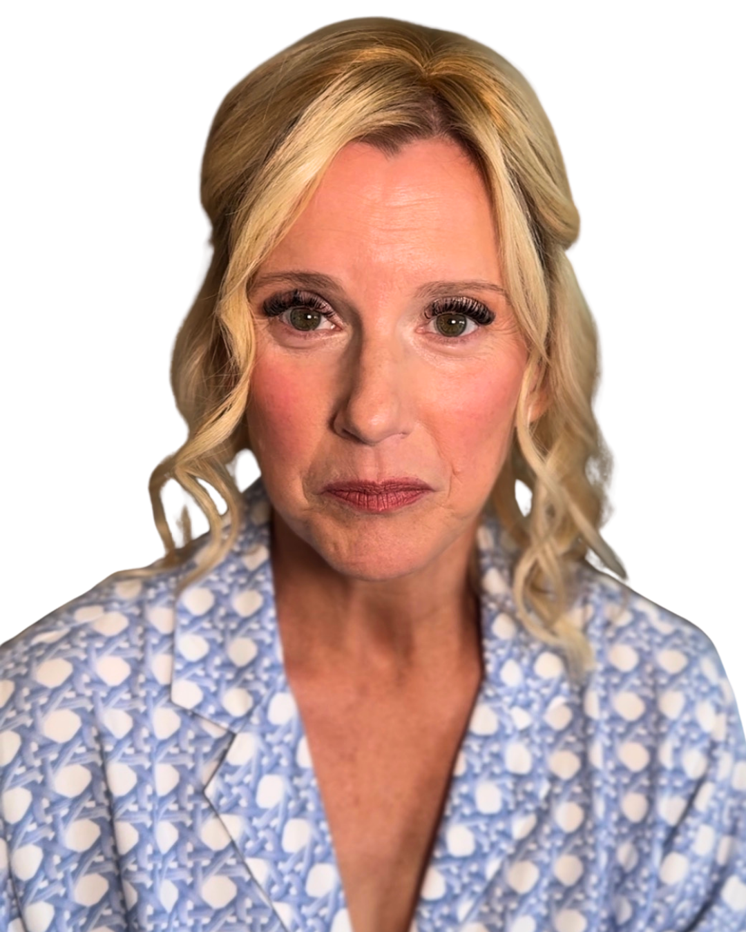 Close-up of a woman with blonde curly hair wearing a blue and white patterned top against a black background.