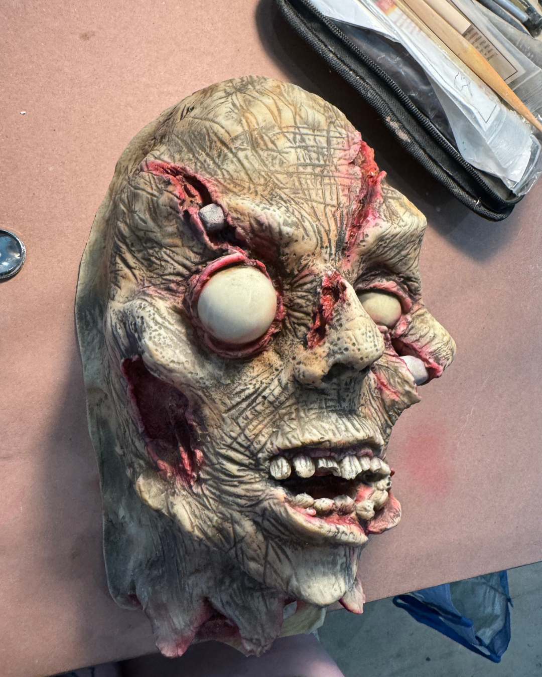 A horror-themed mask or sculpture of a zombie's face with zombie-like features, decayed skin, bulging eyes, and an open mouth. The mask appears to be made of latex or similar material.