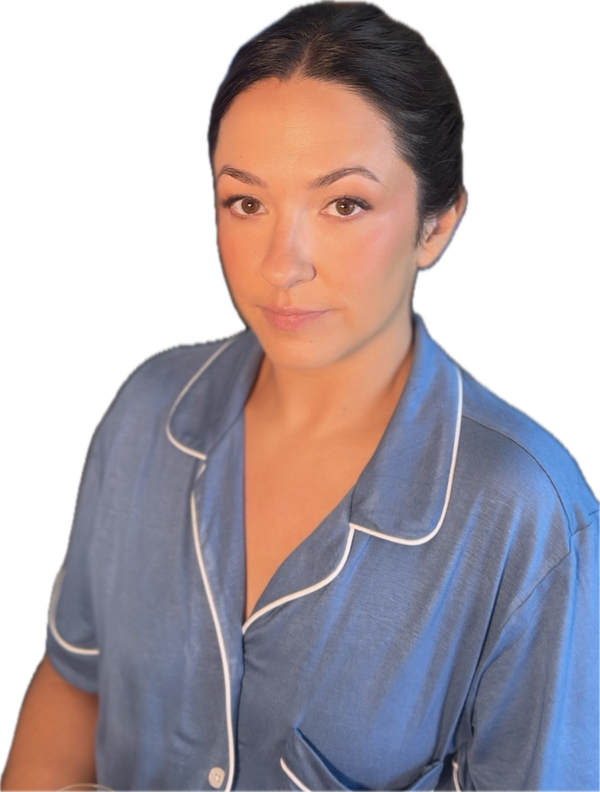 A woman with dark hair in a bun wearing blue pajamas with white piping, looking at the camera with a neutral expression.