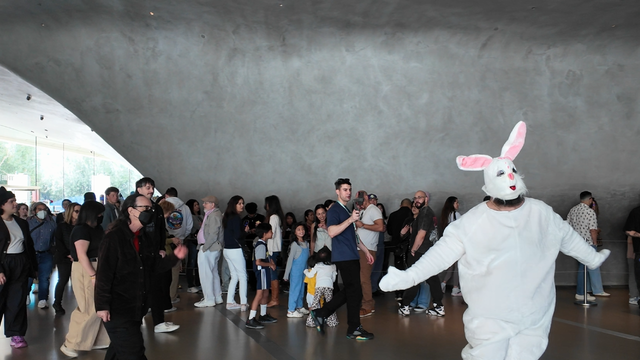 Performance artwork at The Broad taking place inside their cavernous interior space with a large audience watching a performer in a white bunny costume dancing around the space.