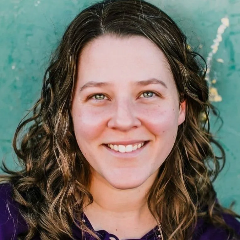 Close-up of a smiling woman with wavy brown hair and light skin, against a turquoise background.