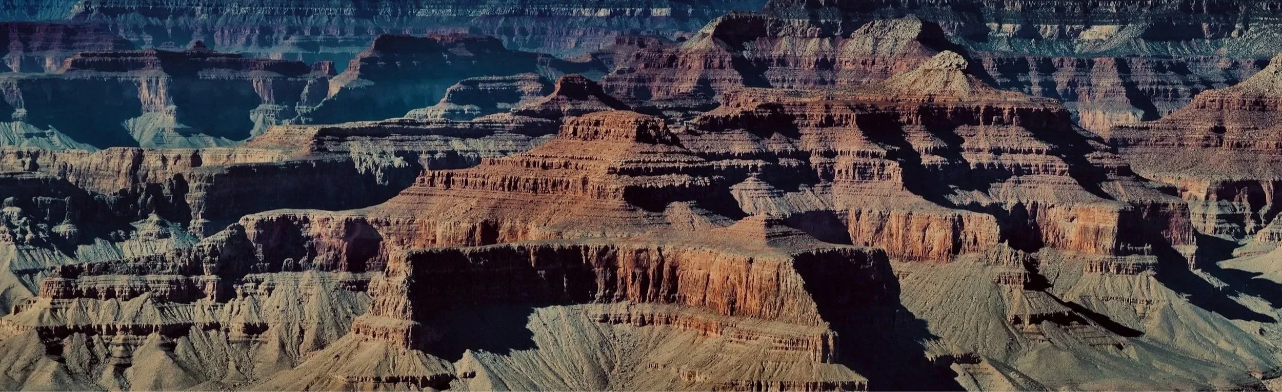 Expansive view of the Grand Canyon with layered red and brown rock formations under a clear sky.